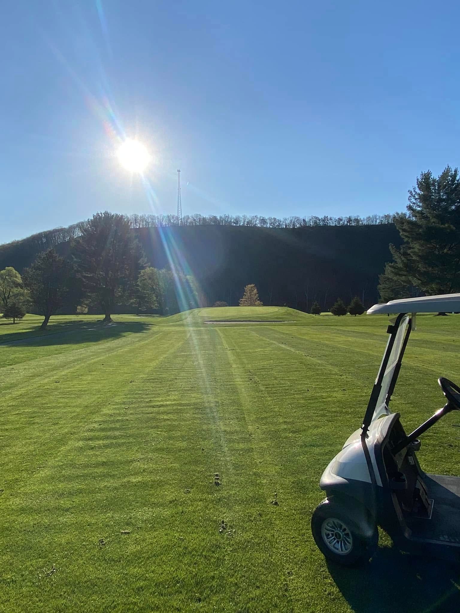 Bright sunny day on a golf course. A golf cart sits in the foreground, green grass stretches towards the green