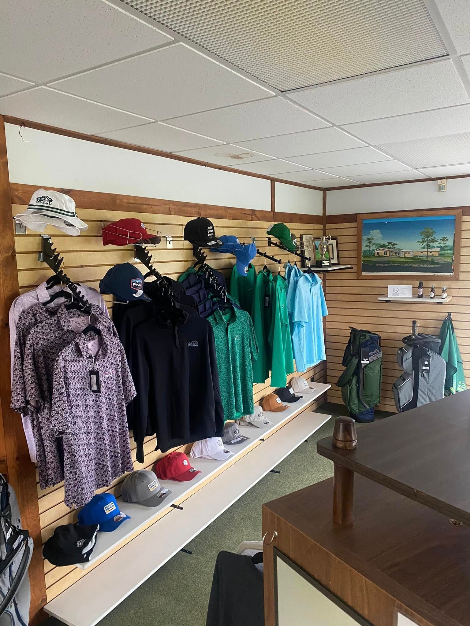 Golf apparel and hats displayed for sale on a store wall. The interior shot includes clothing racks, shelves, and a painting.