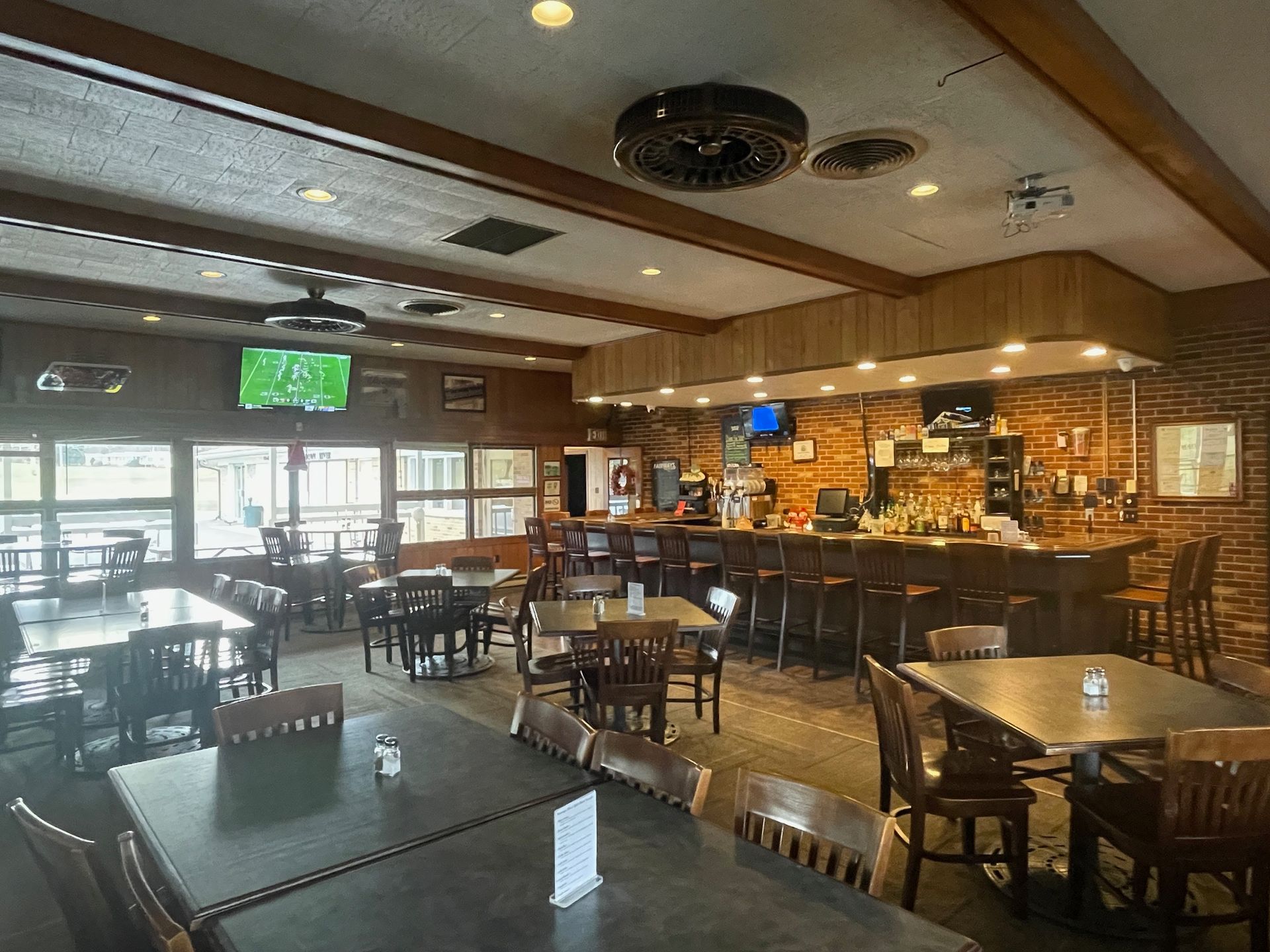 Interior view of a restaurant and bar with tables, chairs, and a wooden bar. A television is mounted on the wall.