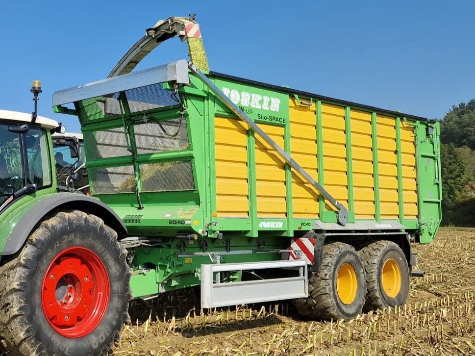 Grüner und gelber Futterwagen wird auf einem Feld mit Erntegut eines Mähdreschers befüllt.