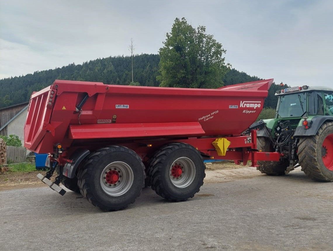 Roter landwirtschaftlicher Anhänger, der im Freien an einen grünen Traktor angehängt ist.