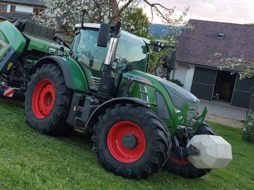 Grüner Fendt-Traktor mit roten Rädern, geparkt auf einem Grashang, im Hintergrund ein Haus.