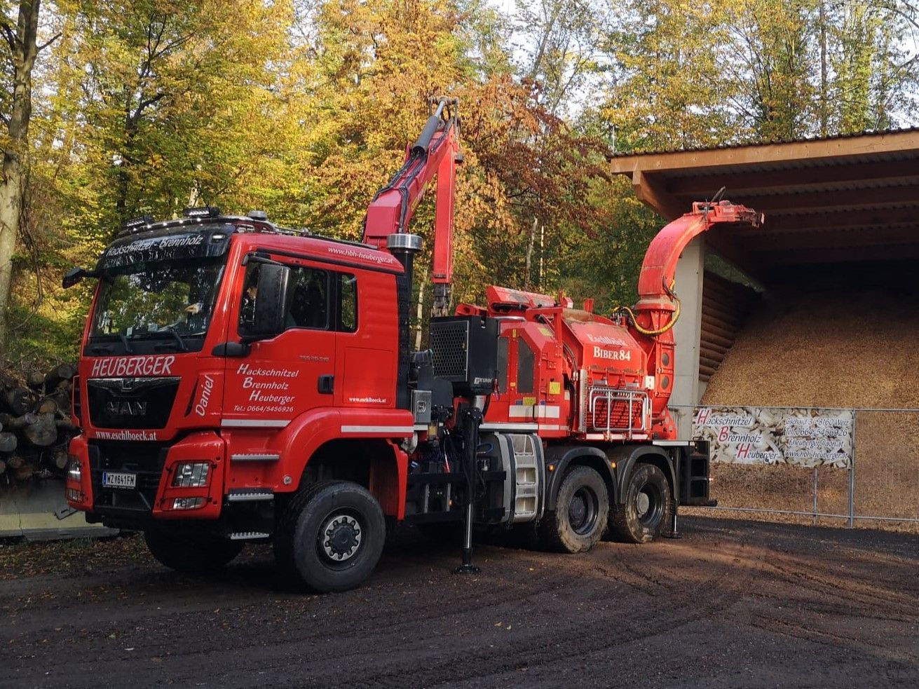 Roter Holzhäcksler-LKW in einer Waldlandschaft, der Holz zu einem Stapel verarbeitet.