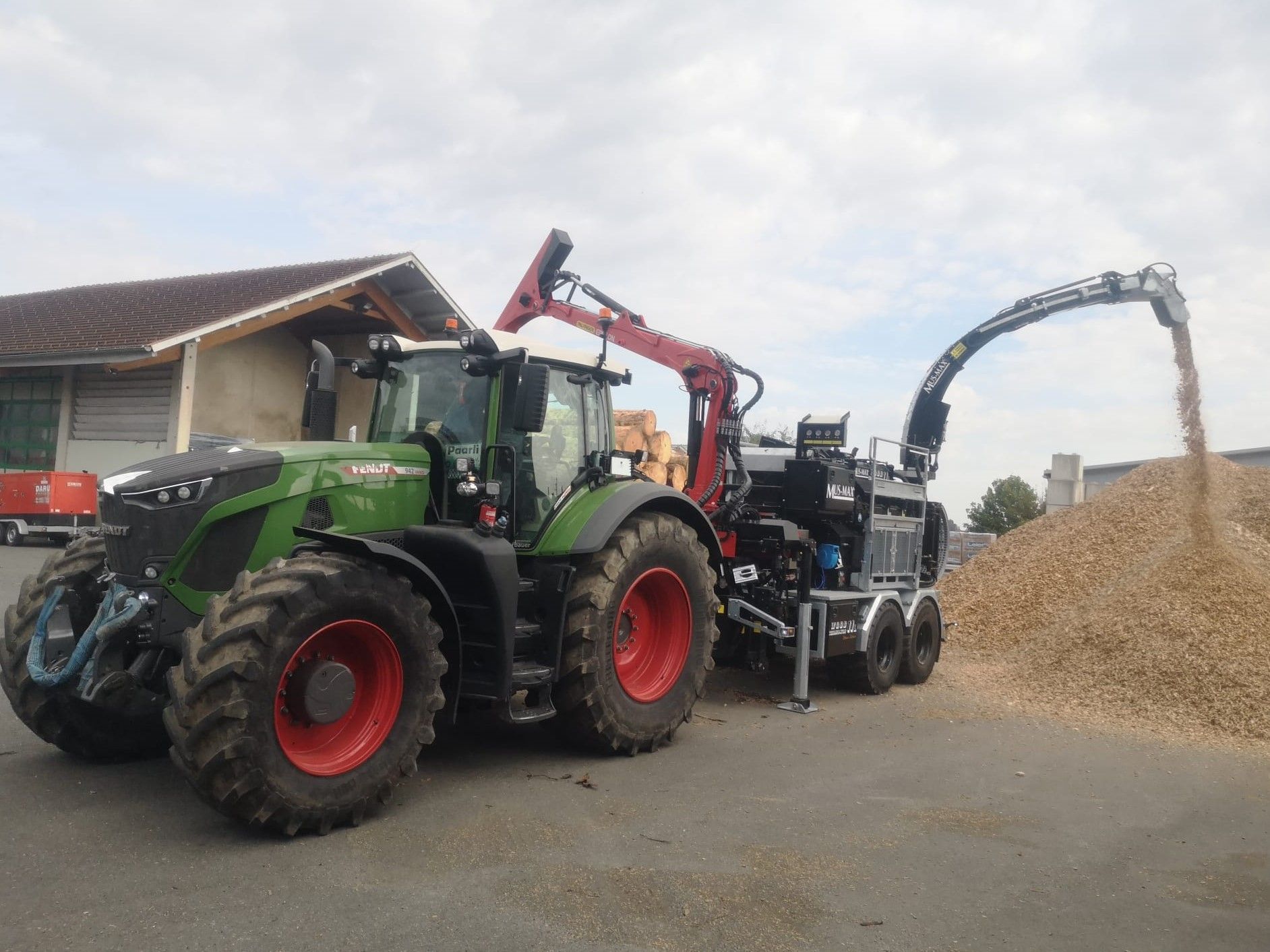 Grüner Traktor mit Holzhäcksler wirft Holzspäne aus.
