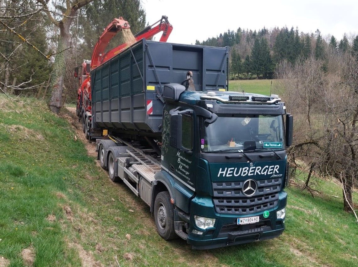 Grüner Mercedes-LKW mit einem Container, der auf einer Rasenfläche mit einem Kranarm beladen wird.