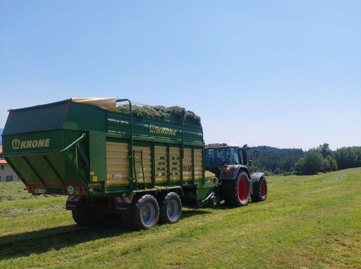 Grüner Krone-Ladewagen, der an einem sonnigen Tag von einem Traktor auf einer Wiese gezogen wird.