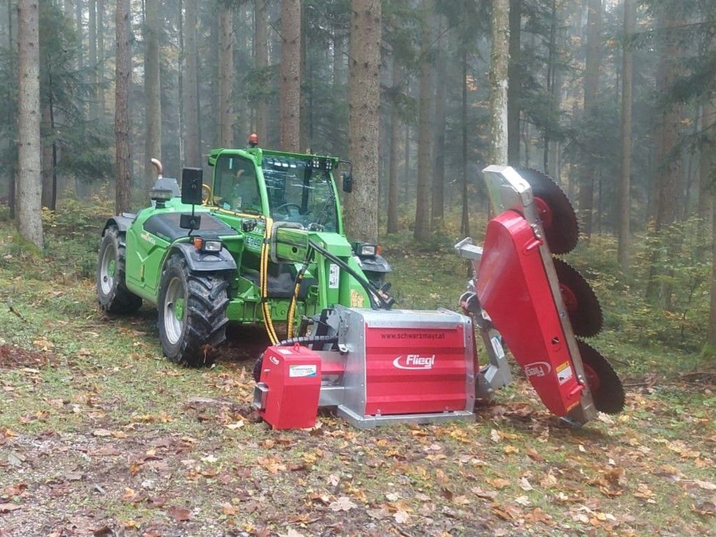 Grüne Forstmaschine mit rotem Anbaugerät im Wald.