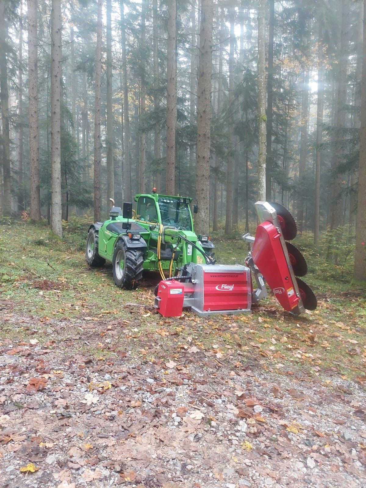 Grüner Traktor mit angebautem roten Forstmulcher auf einer Waldlichtung.