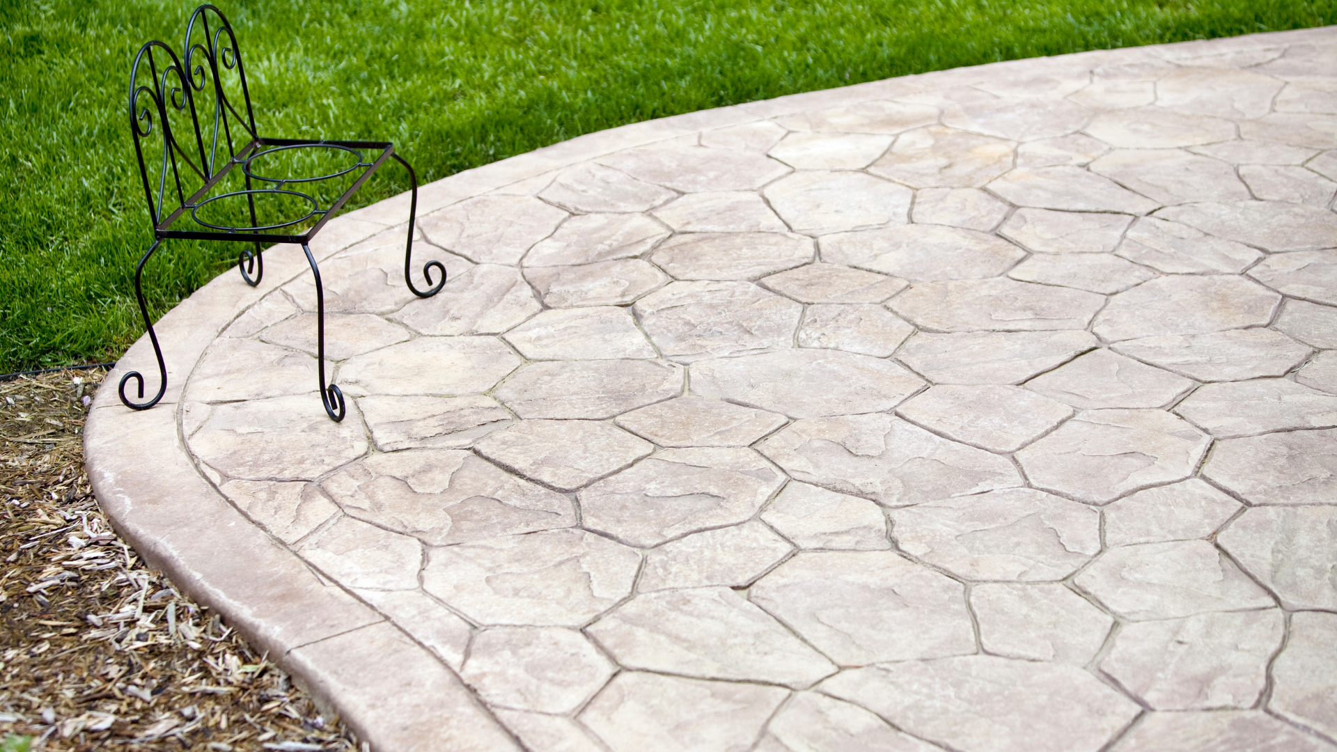 Curved concrete patio beside green grass, with a black metal chair on the left.