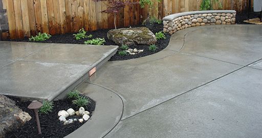 Curved concrete patio and walkway with landscaped rock beds and wooden fence