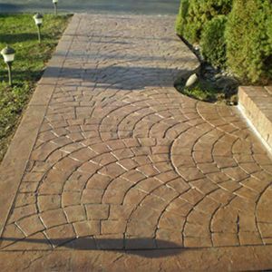 Curved brick-paved walkway bordered by grass and shrubs in bright sunlight