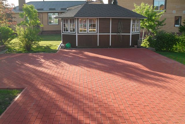 Red paved patio leading to a small brown gazebo in a sunny backyard.