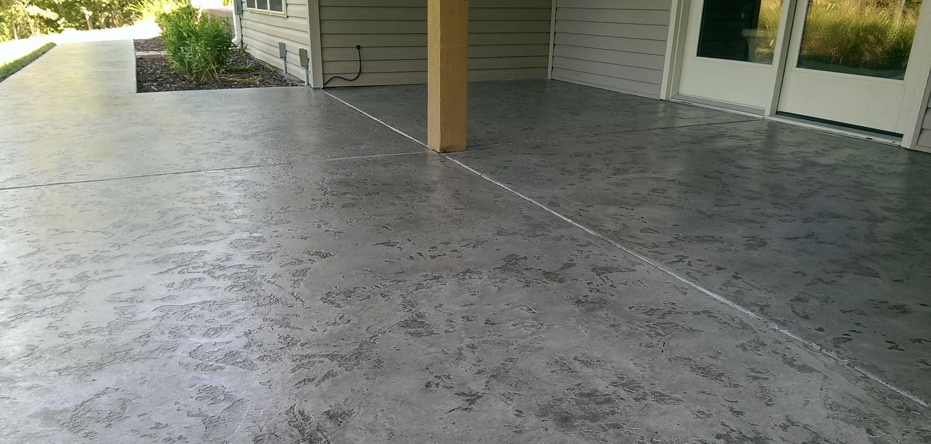 Covered concrete patio with a central support post and house siding in the background
