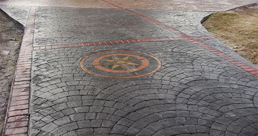 Cobblestone walkway with a circular orange symbol painted on the pavement near a curb and grassy edge
