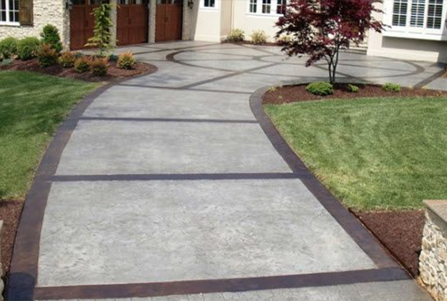 Curved concrete walkway with dark border leading to a house entrance and landscaped front yard