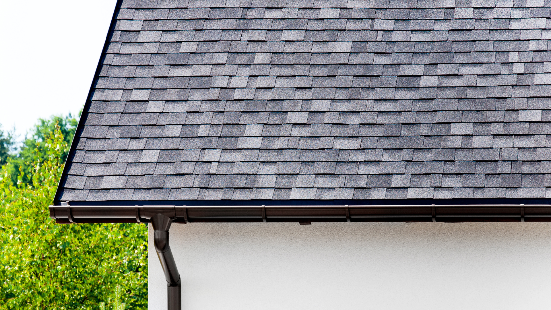 A close up of a roof with shingles and a gutter on a house.