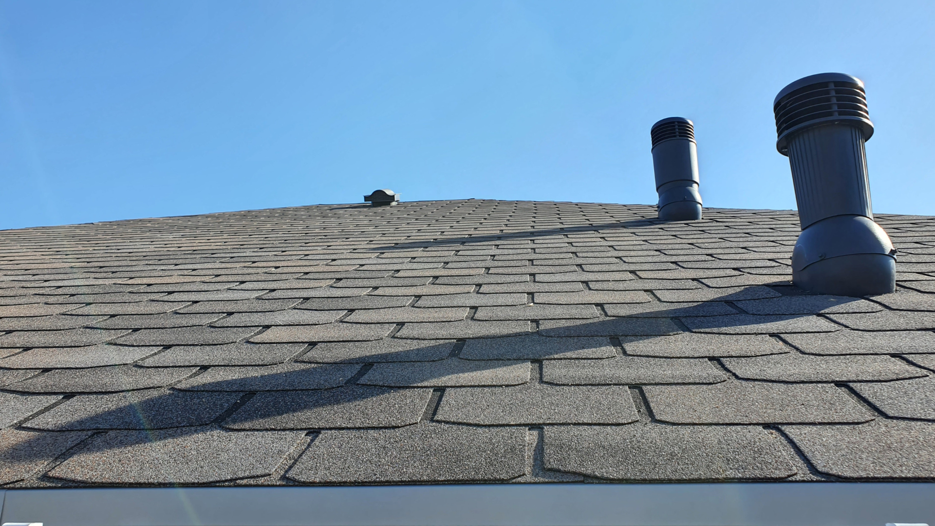 A roof with two chimneys on it and a blue sky in the background.