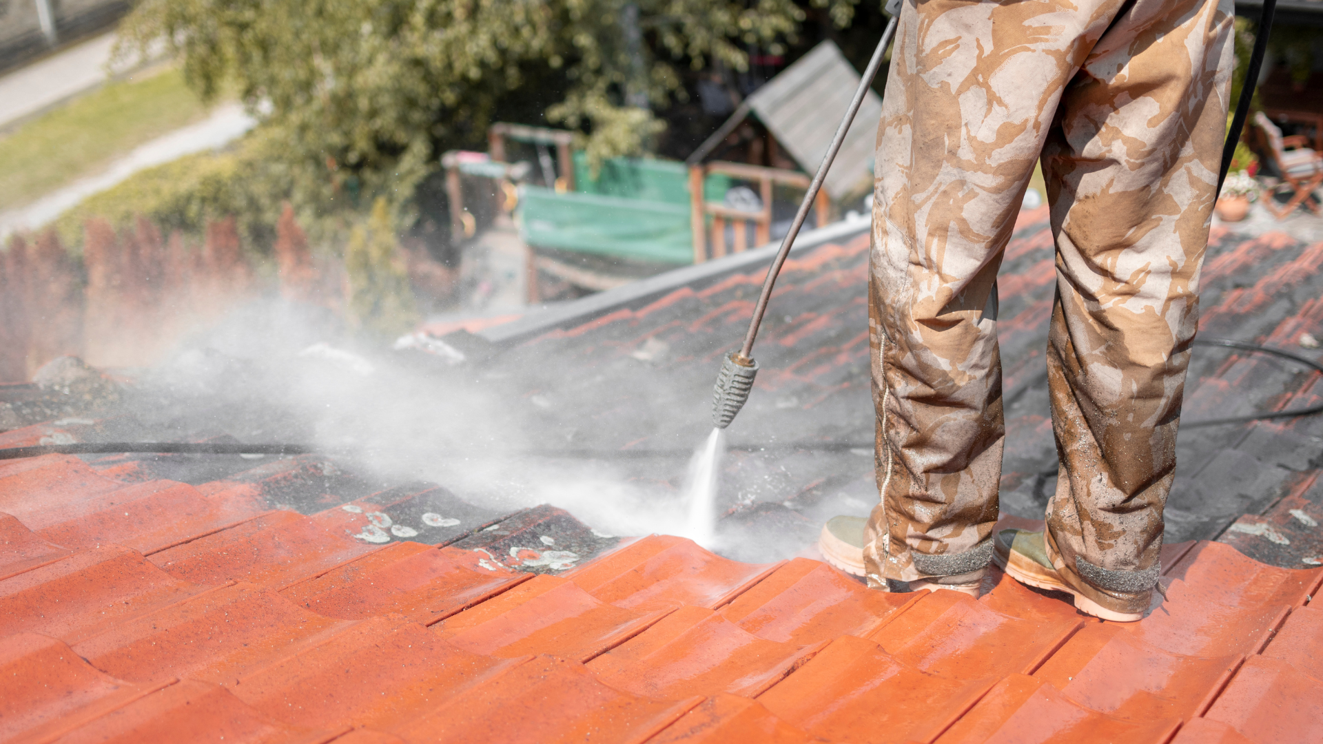 A man is cleaning a roof with a high pressure washer.