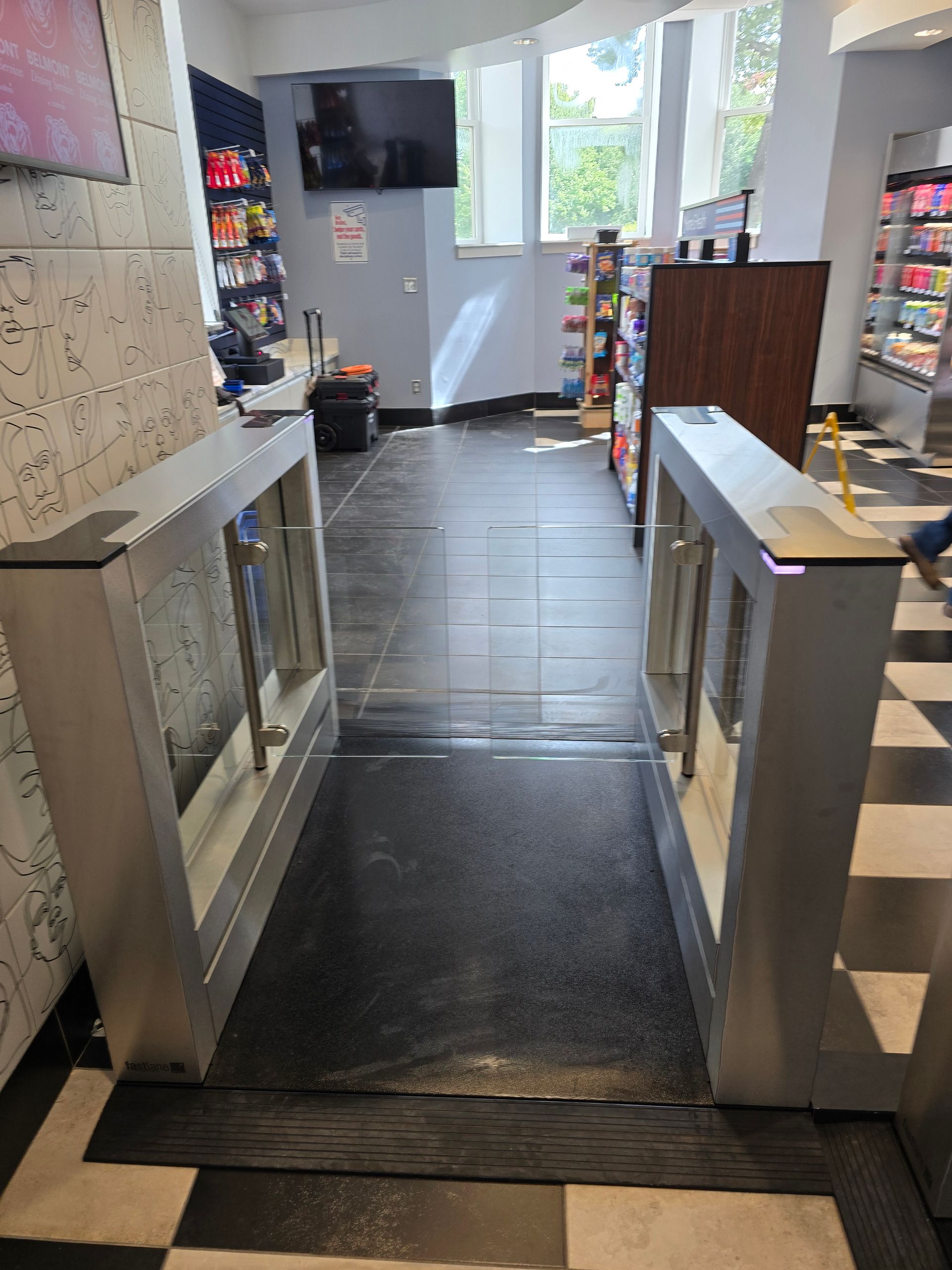 Turnstile entrance to a store with black and white checkered floor and shelves of products.
