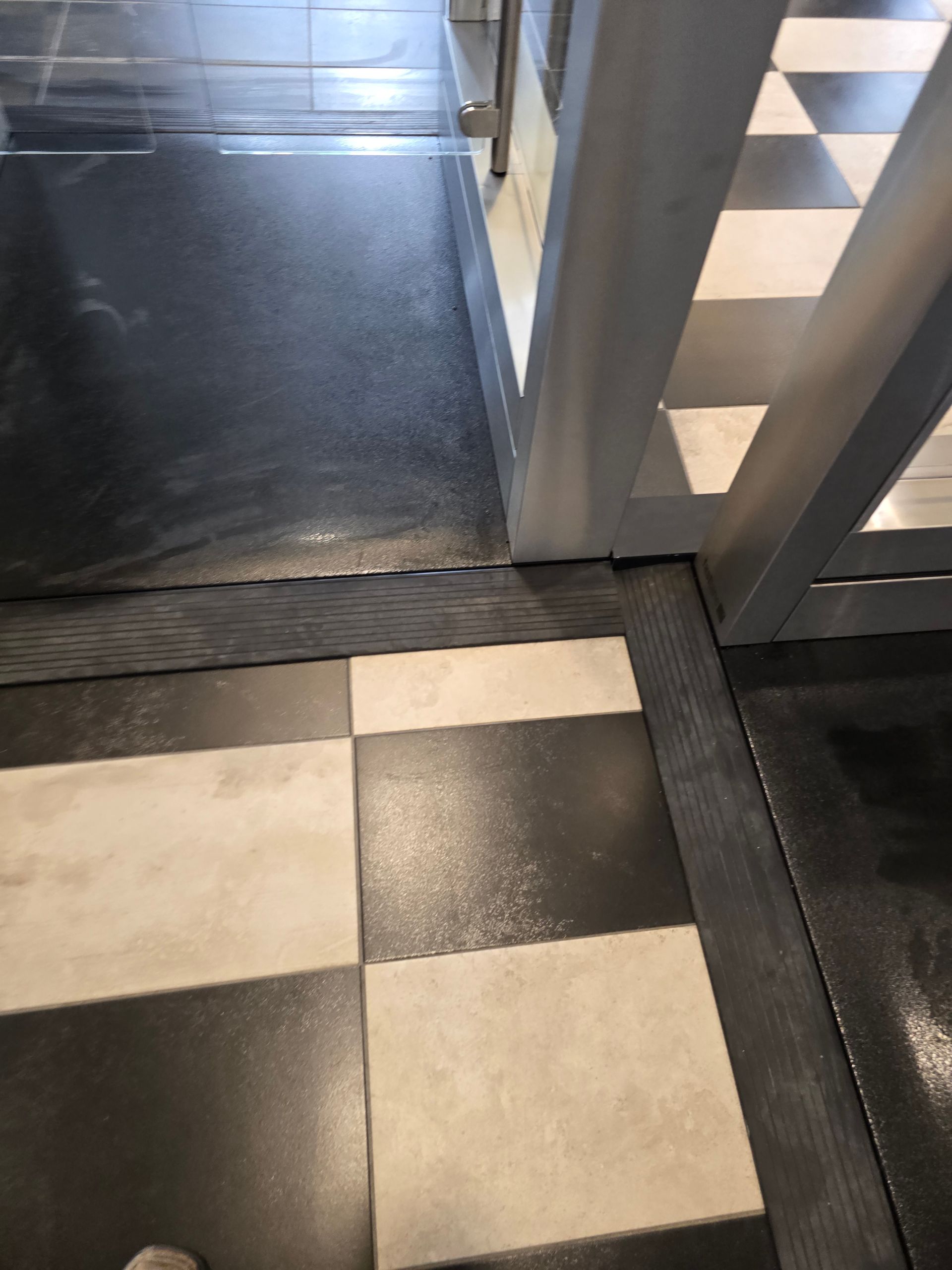 Black and white checkered tile floor transitions to dark floor, with a metal frame in the corner.