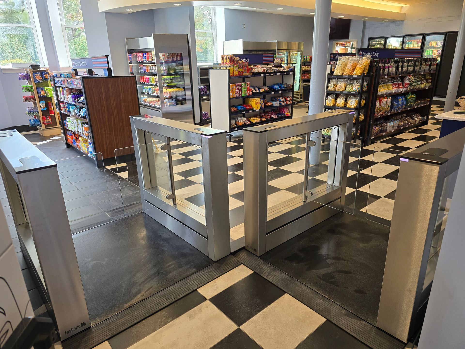 Convenience store interior with entry turnstiles, shelves of snacks and drinks, black and white checkered floor.