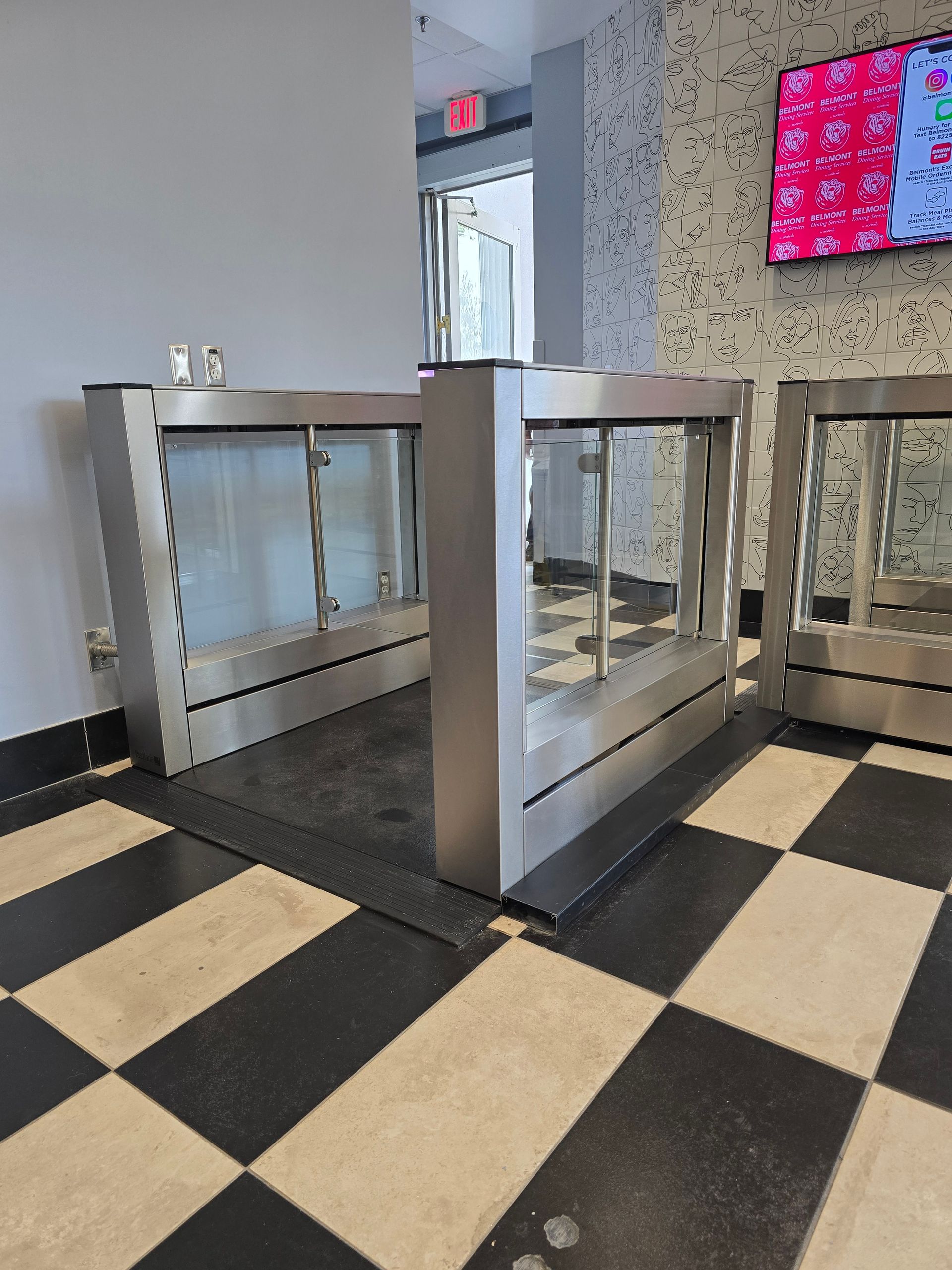 Stainless steel food display cases on checkered floor. 