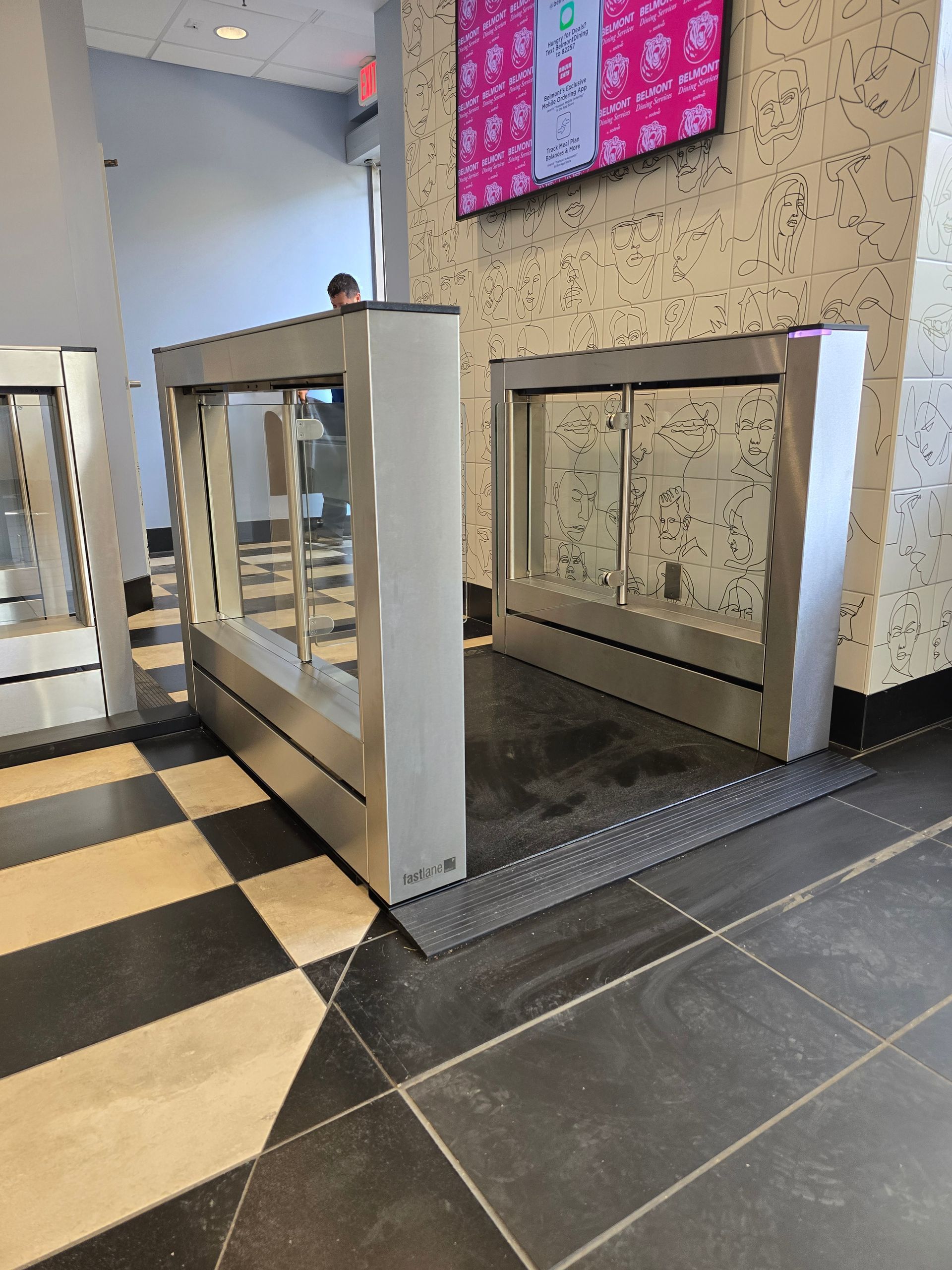 Two silver turnstiles on a checkered floor, one open for access.