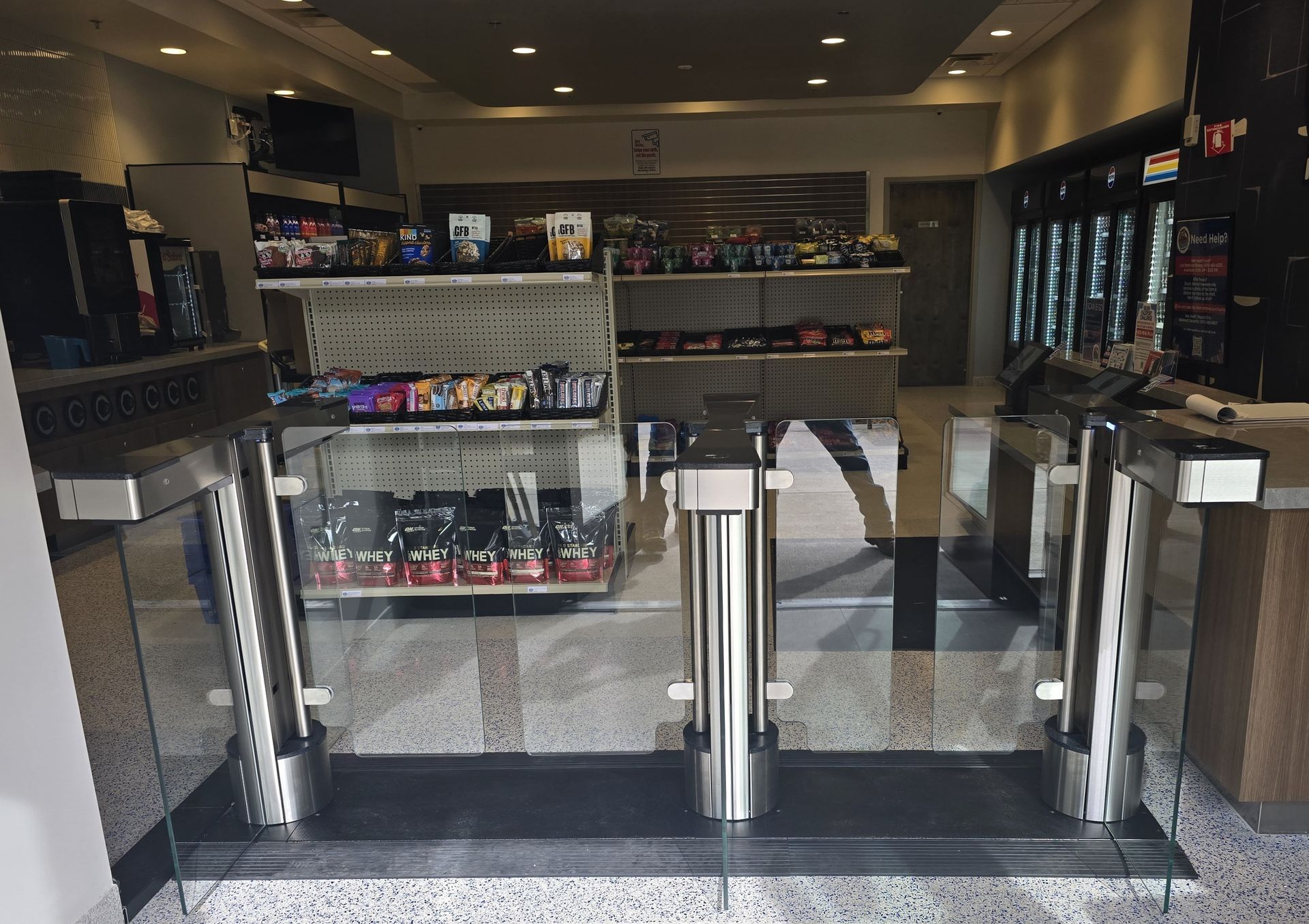 Convenience store entrance with a turnstile and shelves stocked with snacks and drinks.