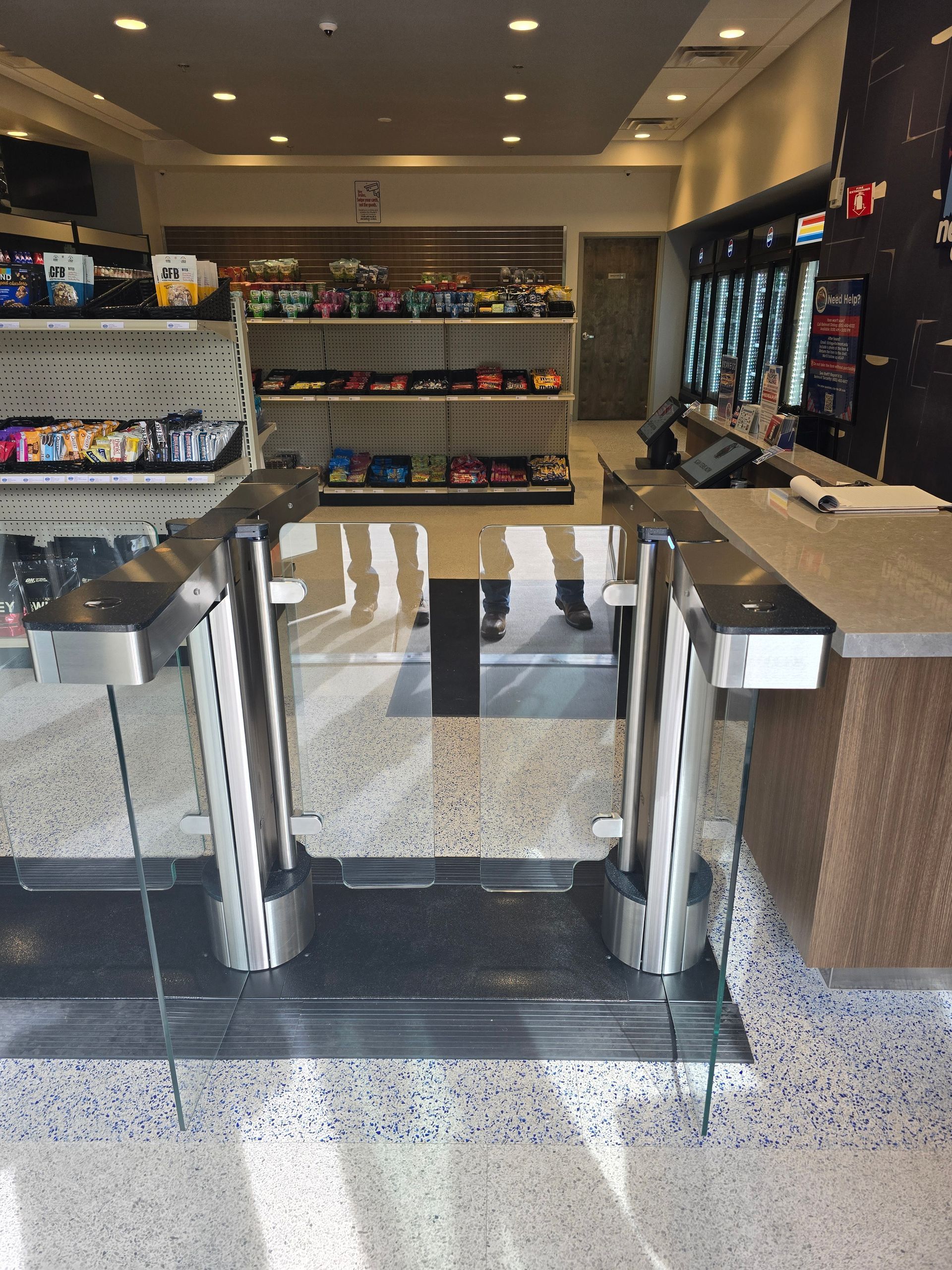 Entrance to a store with stainless steel turnstiles, shelves of products, and a counter.