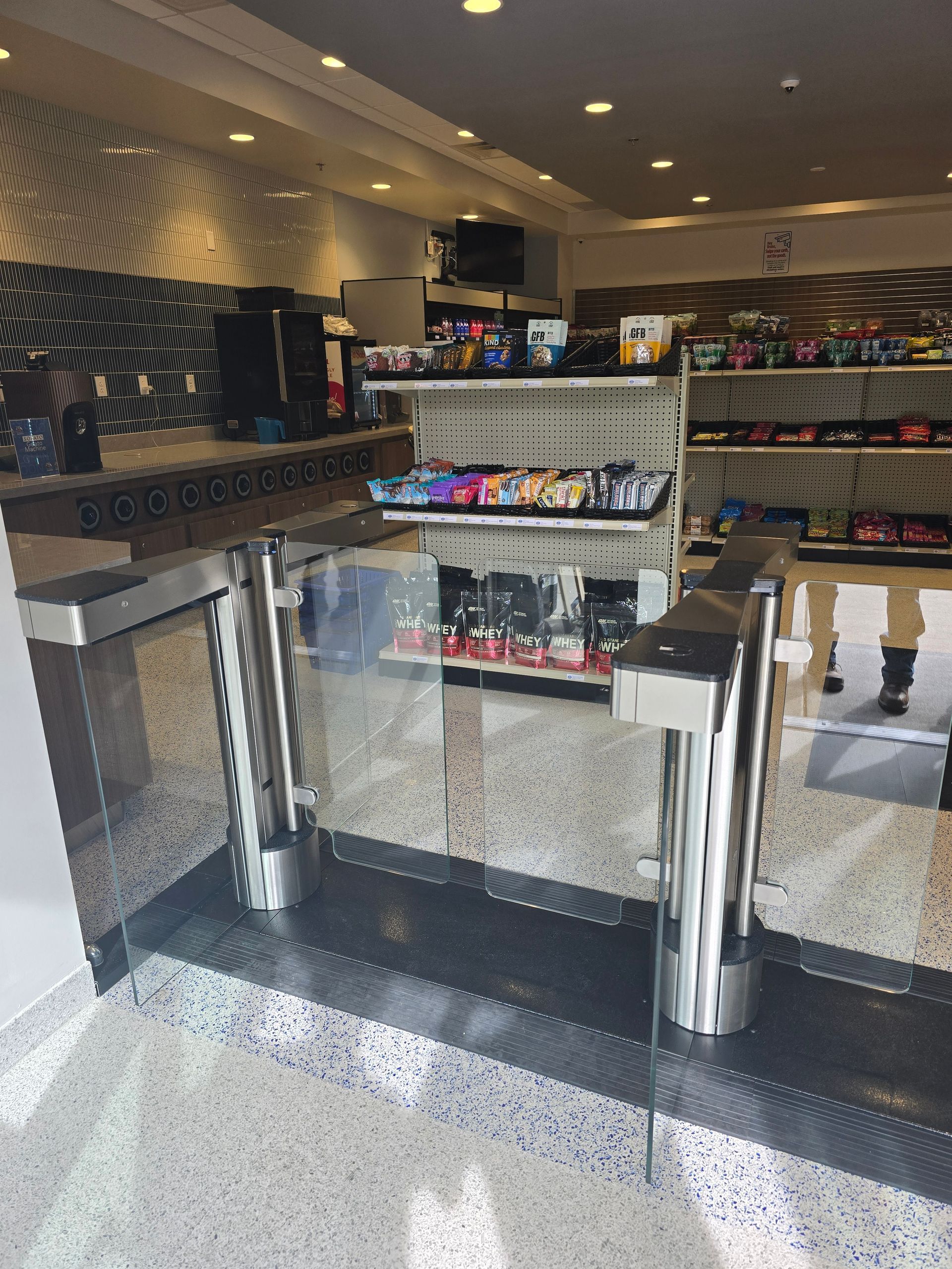 Entrance with security turnstile to a store; shelves with products are visible inside.