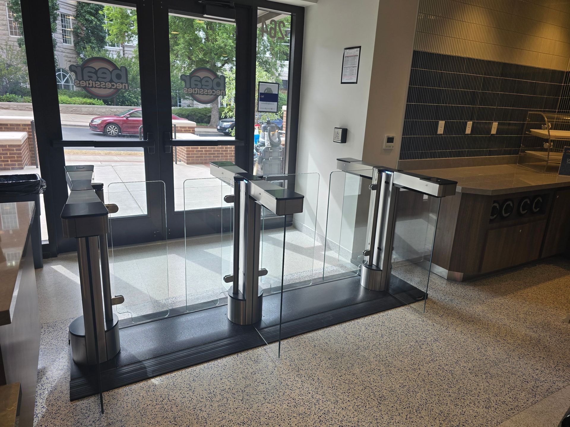 Entrance with turnstiles, glass doors, and speckled flooring. 