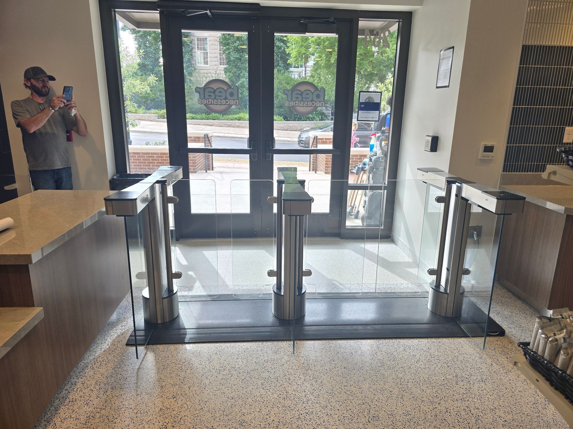 Interior shot with glass turnstiles at a doorway, counter on left and a person on left.