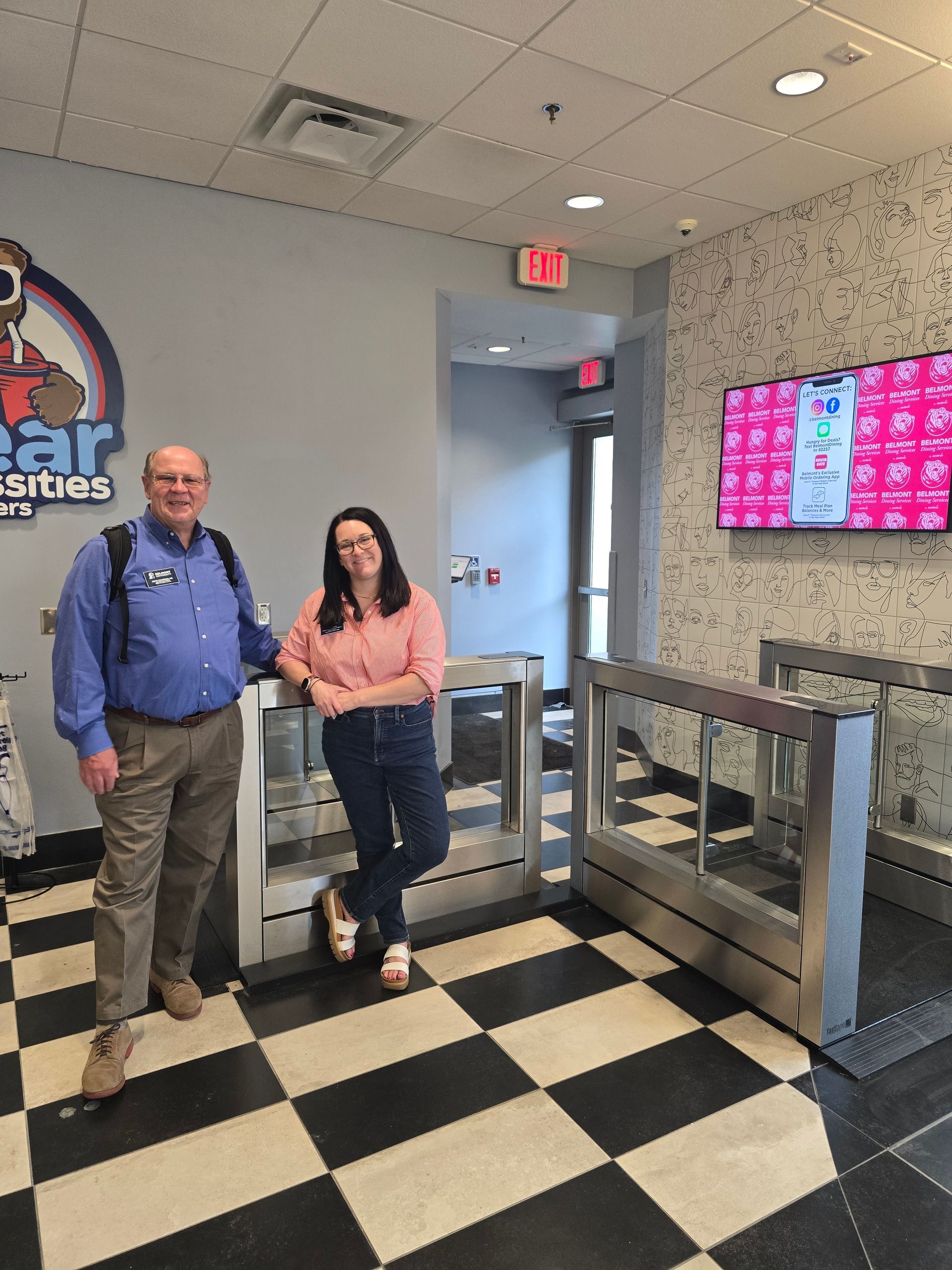 Two people pose by turnstiles with a checkered floor.