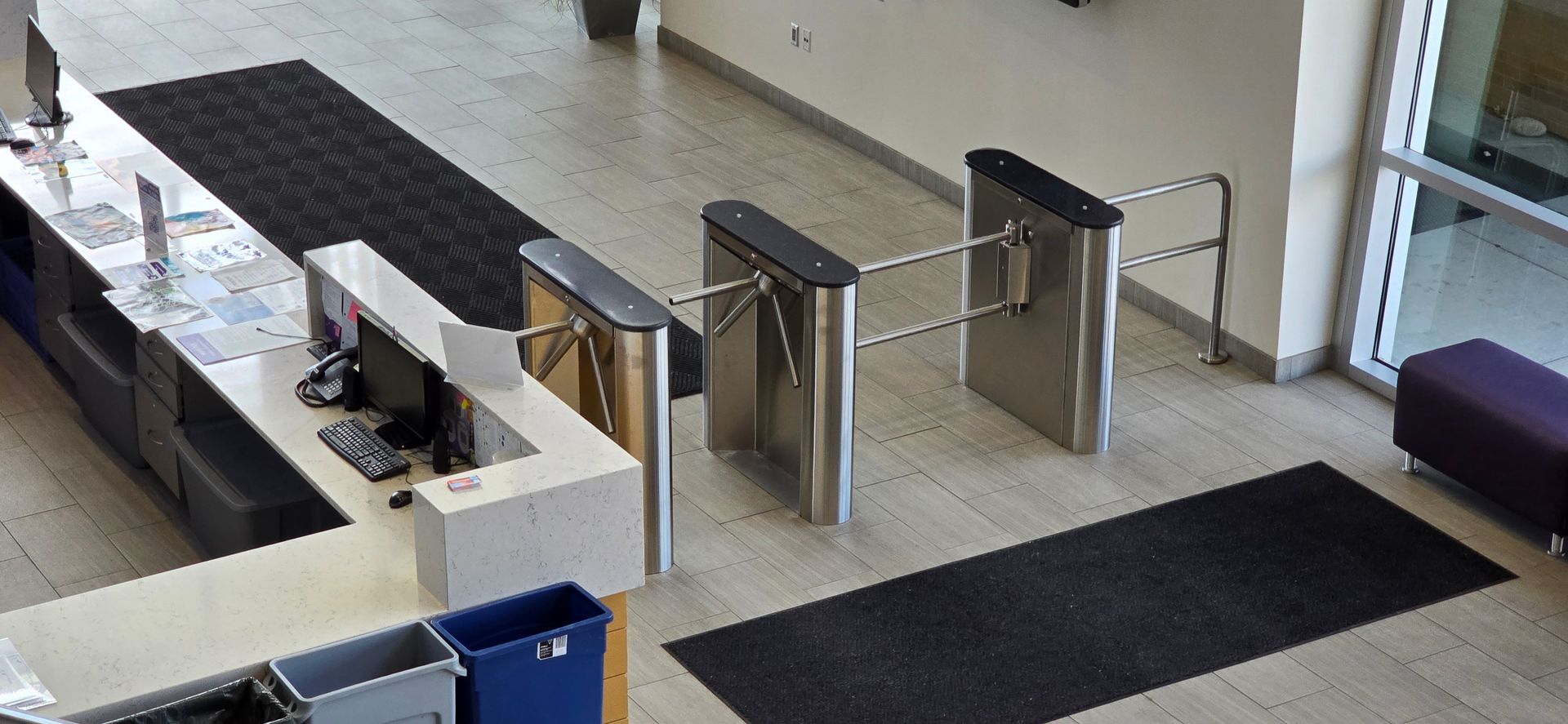 An aerial view of a lobby with security turnstiles, a reception desk, and a dark rug.