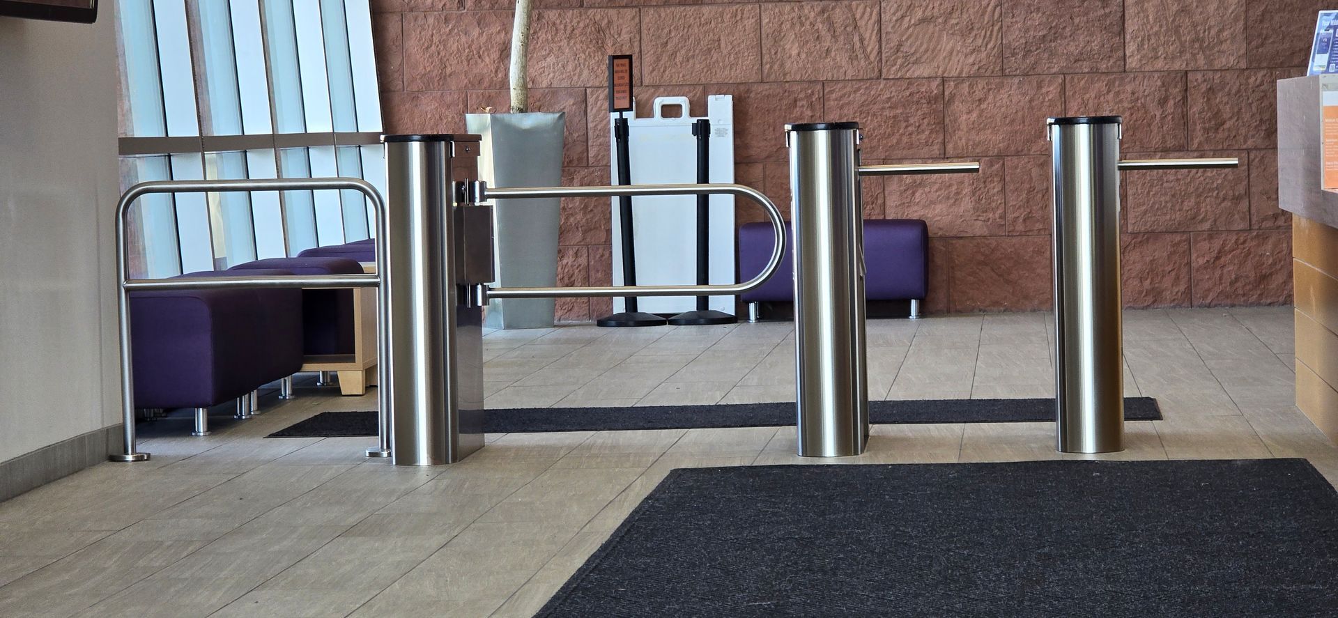 Stainless steel turnstiles in a building entrance, set on a dark mat.
