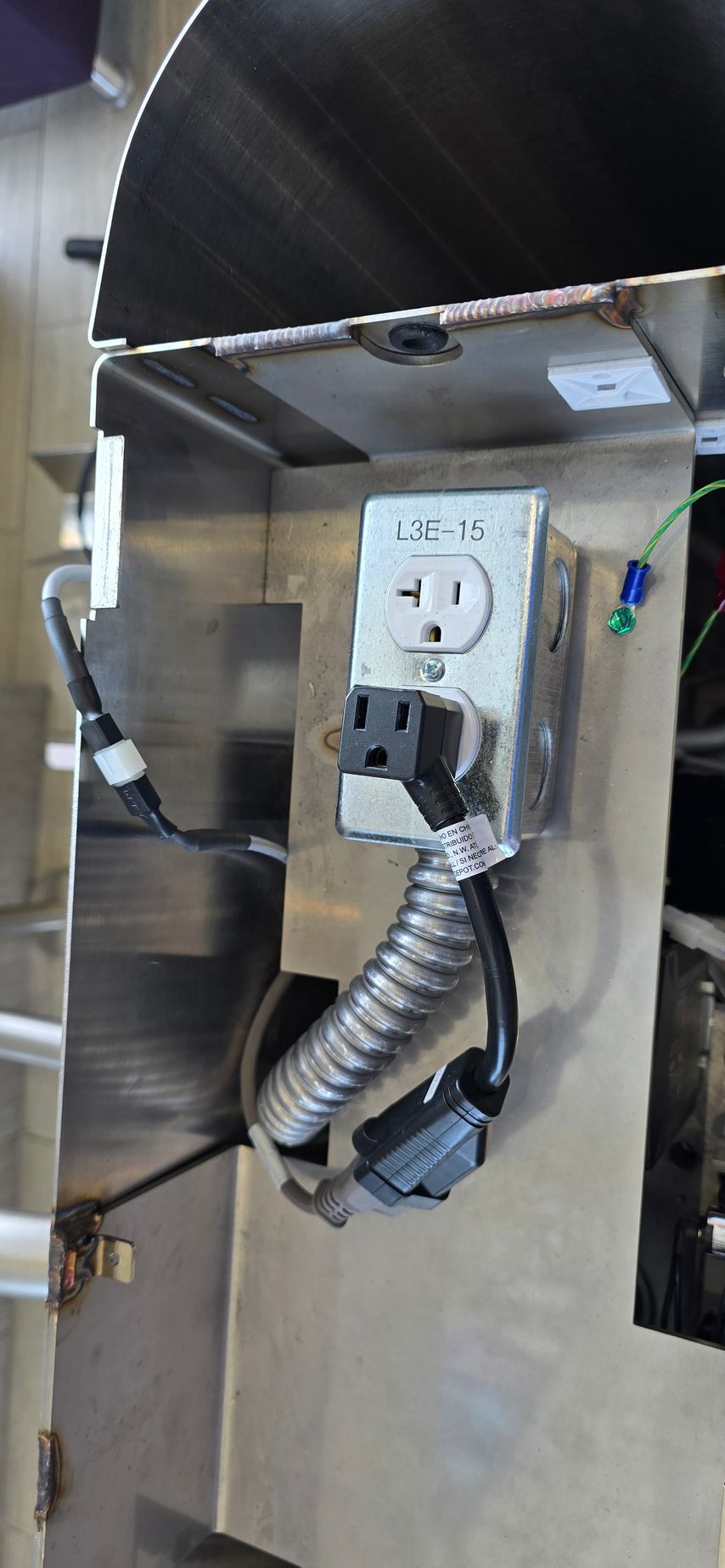 A metal outlet and power cord are installed on a stainless steel surface.