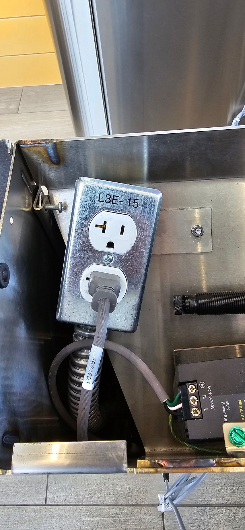 An electrical outlet with a cord plugged in, mounted on a stainless steel surface.