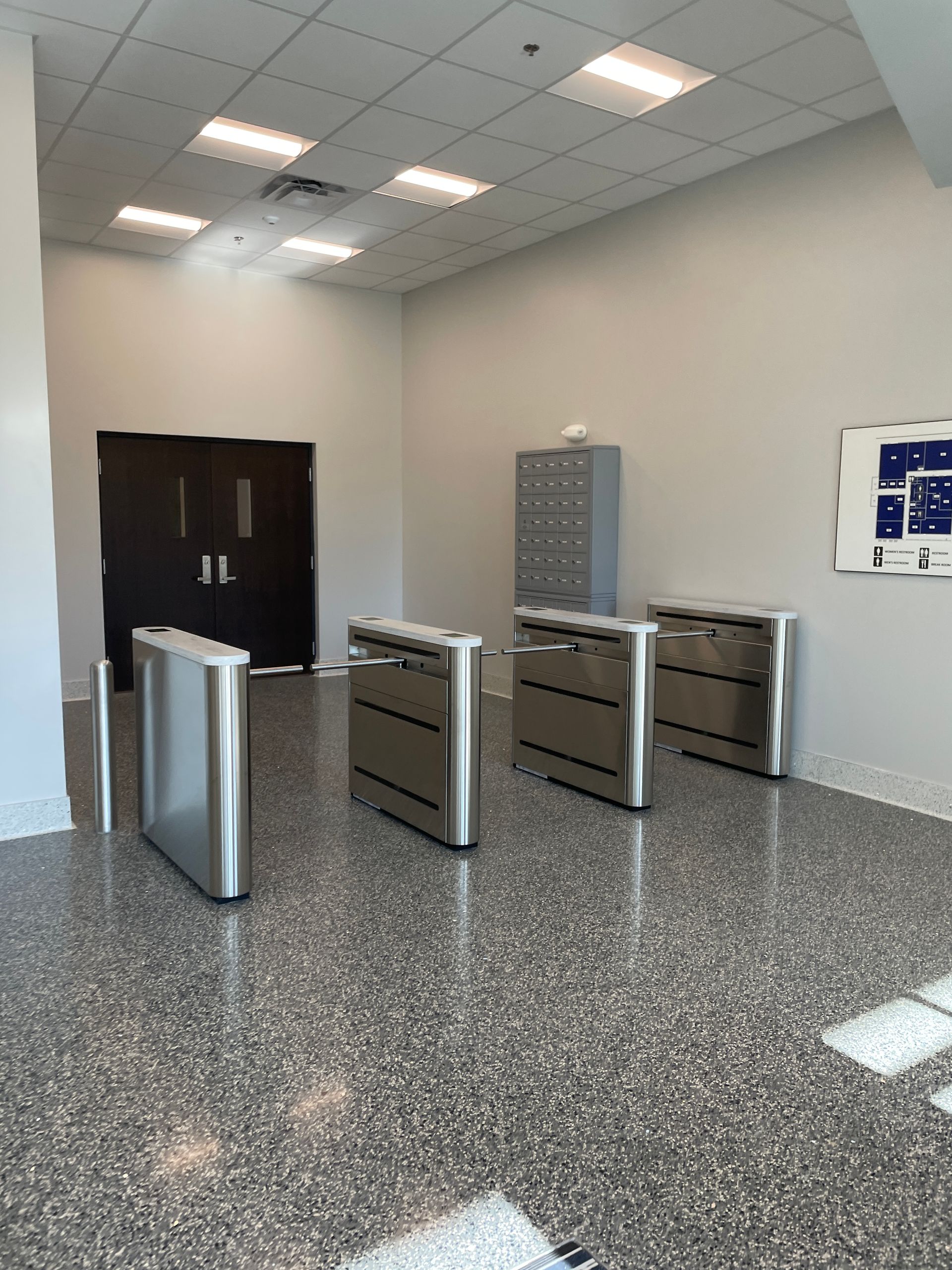 A lobby with security turnstiles and a door, next to a filing cabinet and a building layout diagram.
