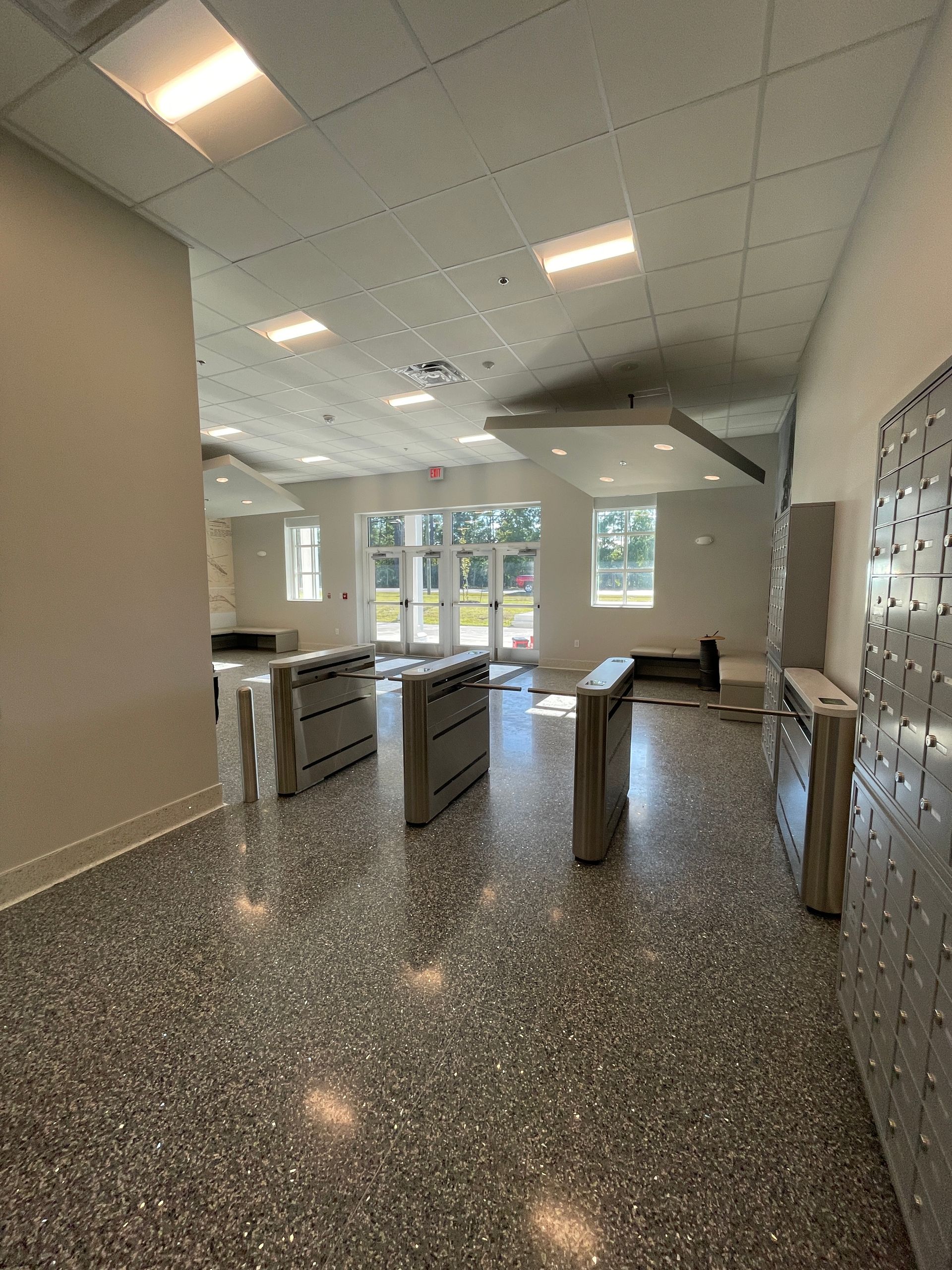 Hallway with speckled floor, security turnstiles, and doors to outside.