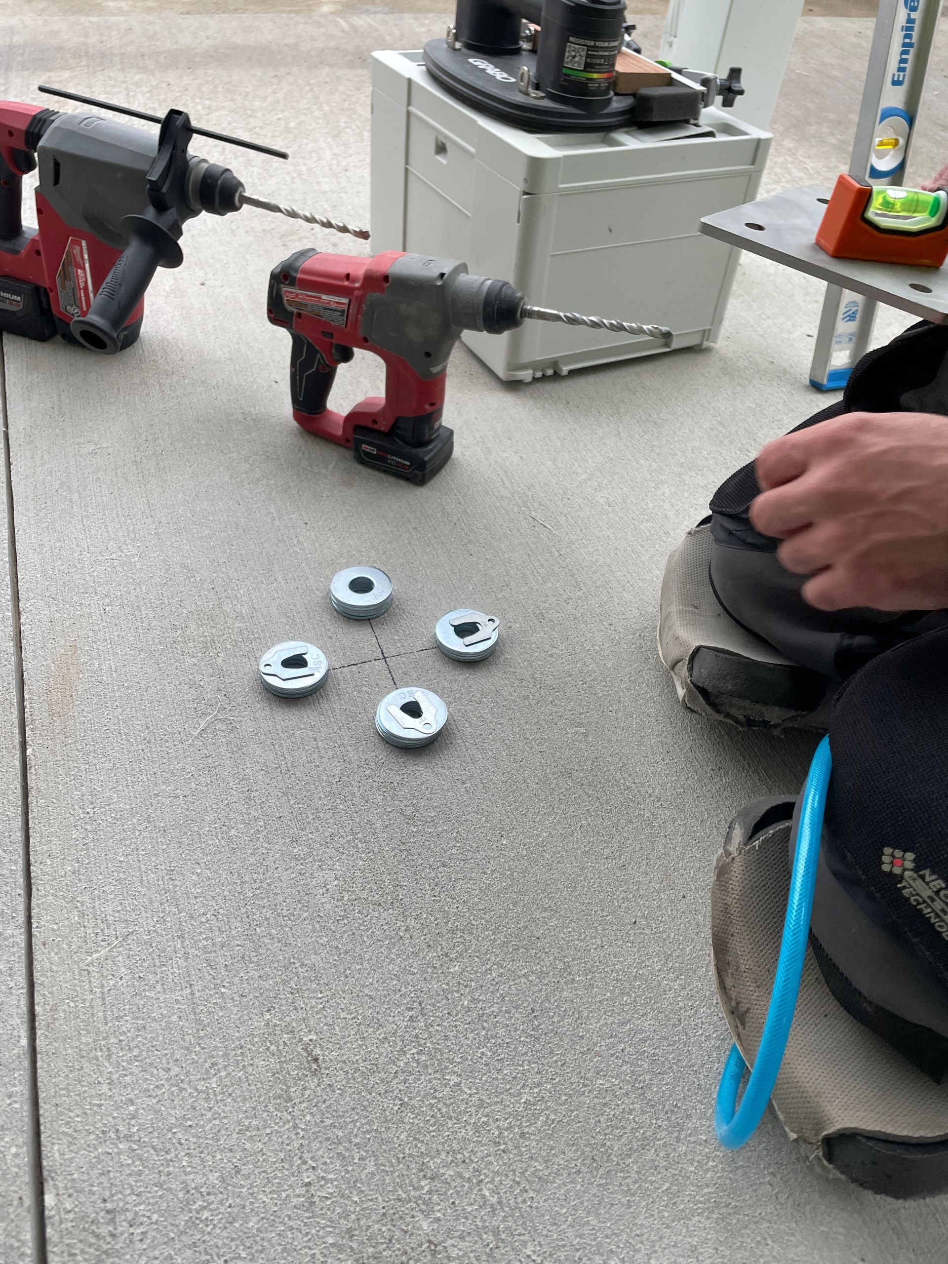 Drills and washers on concrete, tools in background, a hand reaches toward the washers.