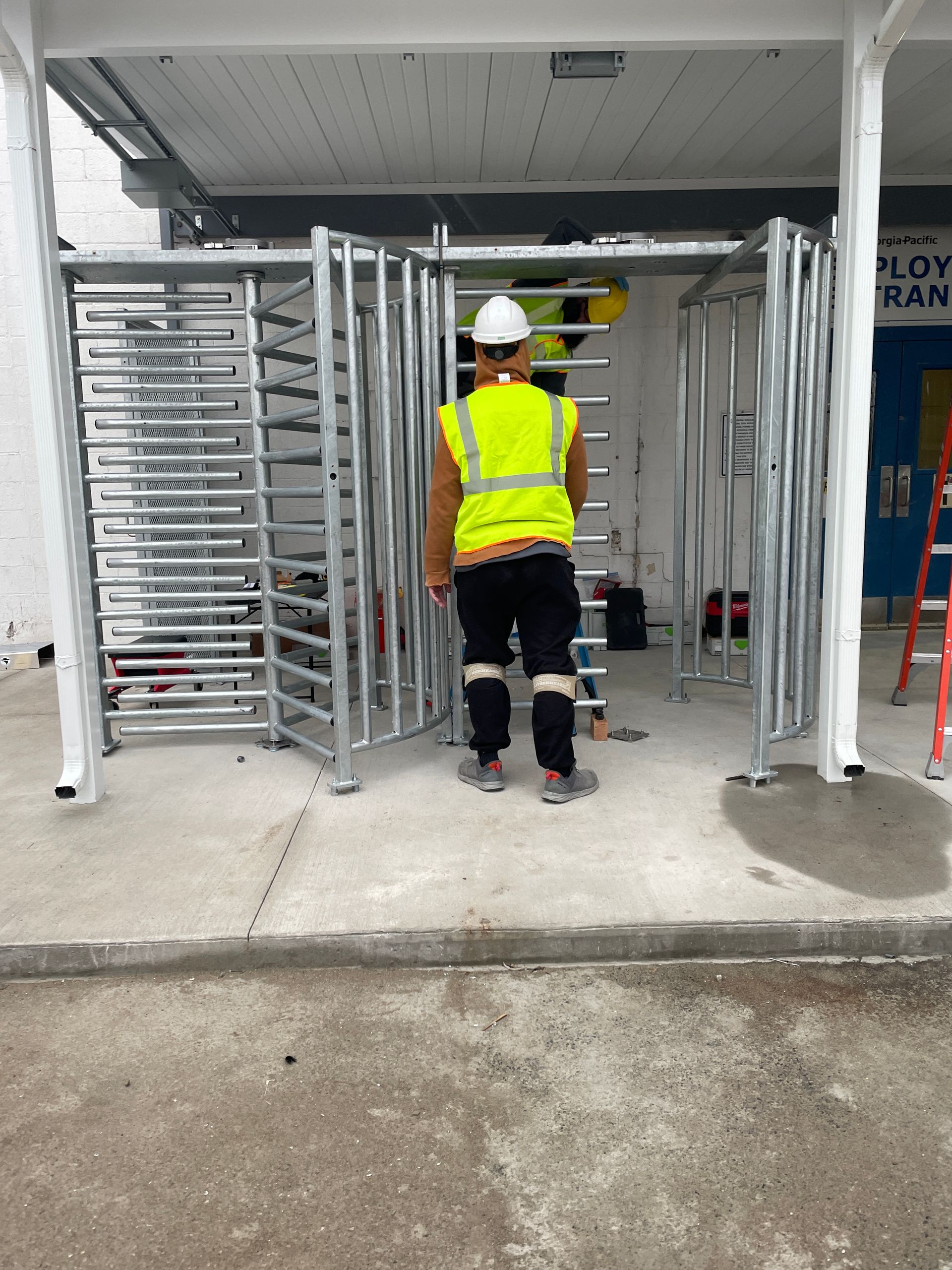 Person in safety vest and hard hat stands near a metal turnstile.