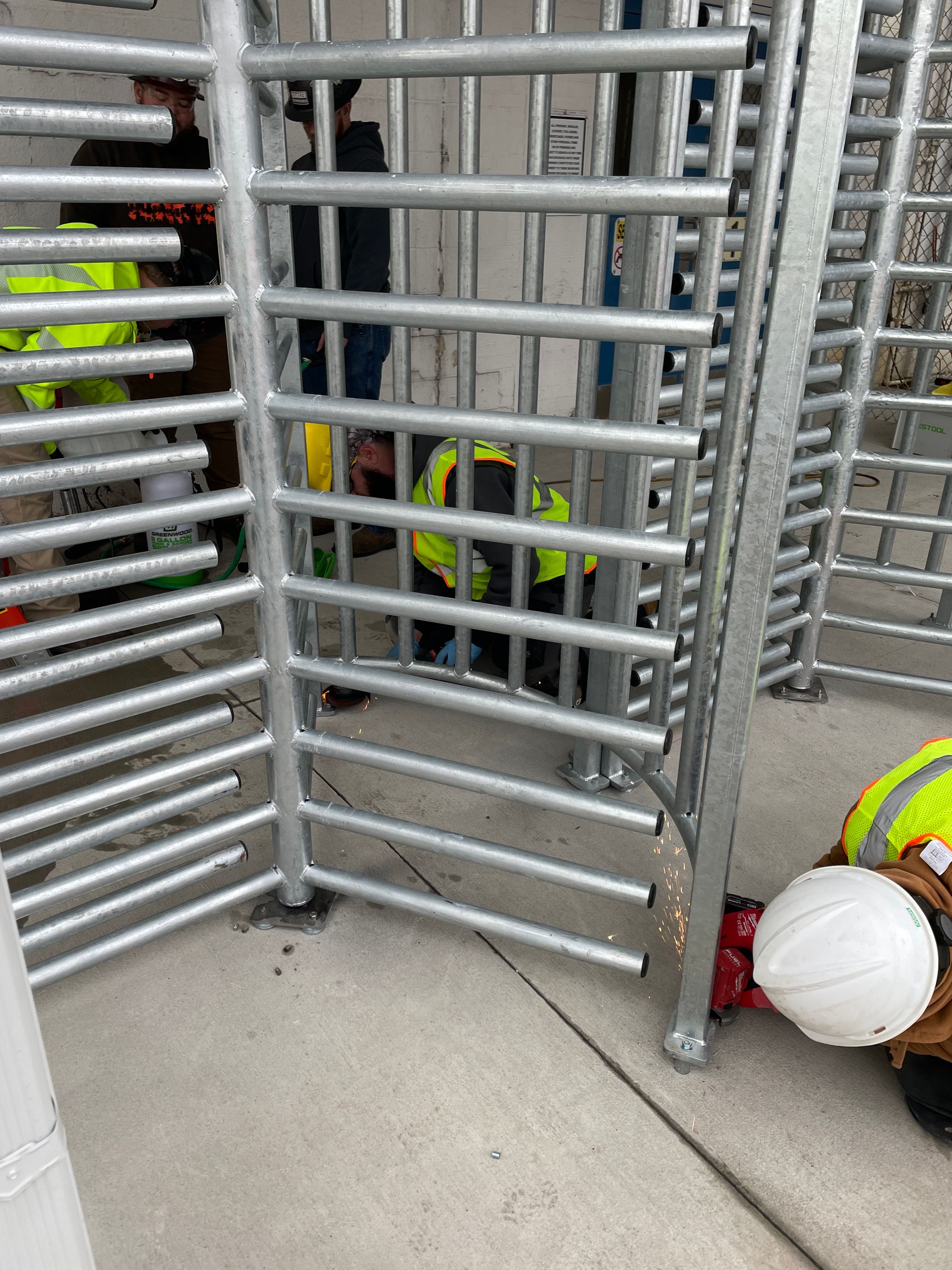 Workers in safety vests installing metal turnstile on concrete.