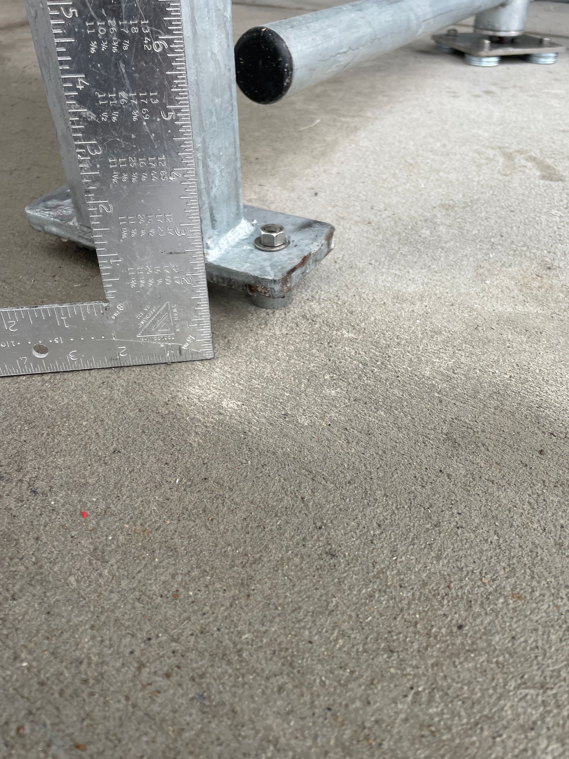 Metal scaffolding base on concrete with a ruler measuring its height.