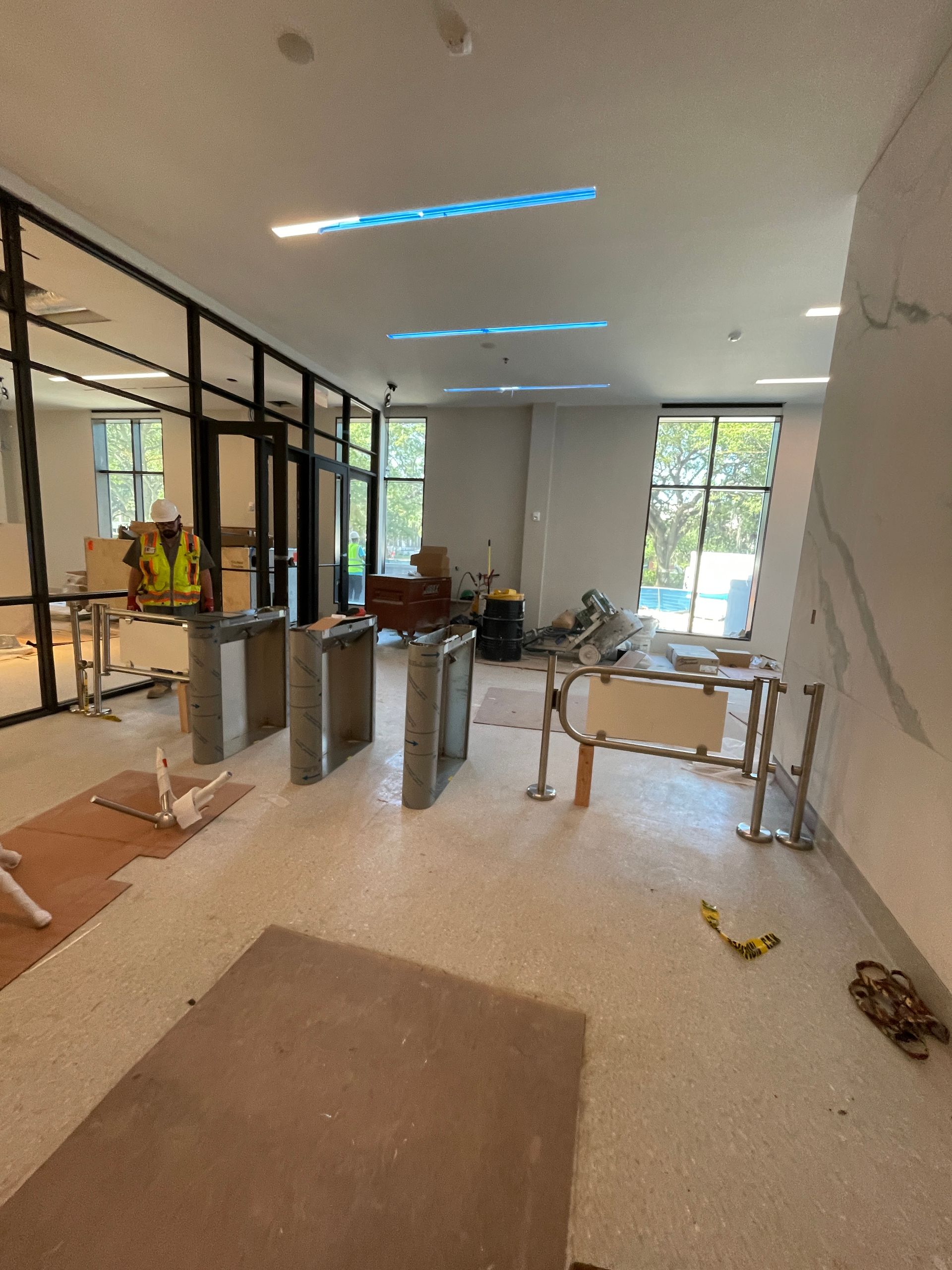 Construction site interior with turnstiles, glass walls, and a light-colored floor.