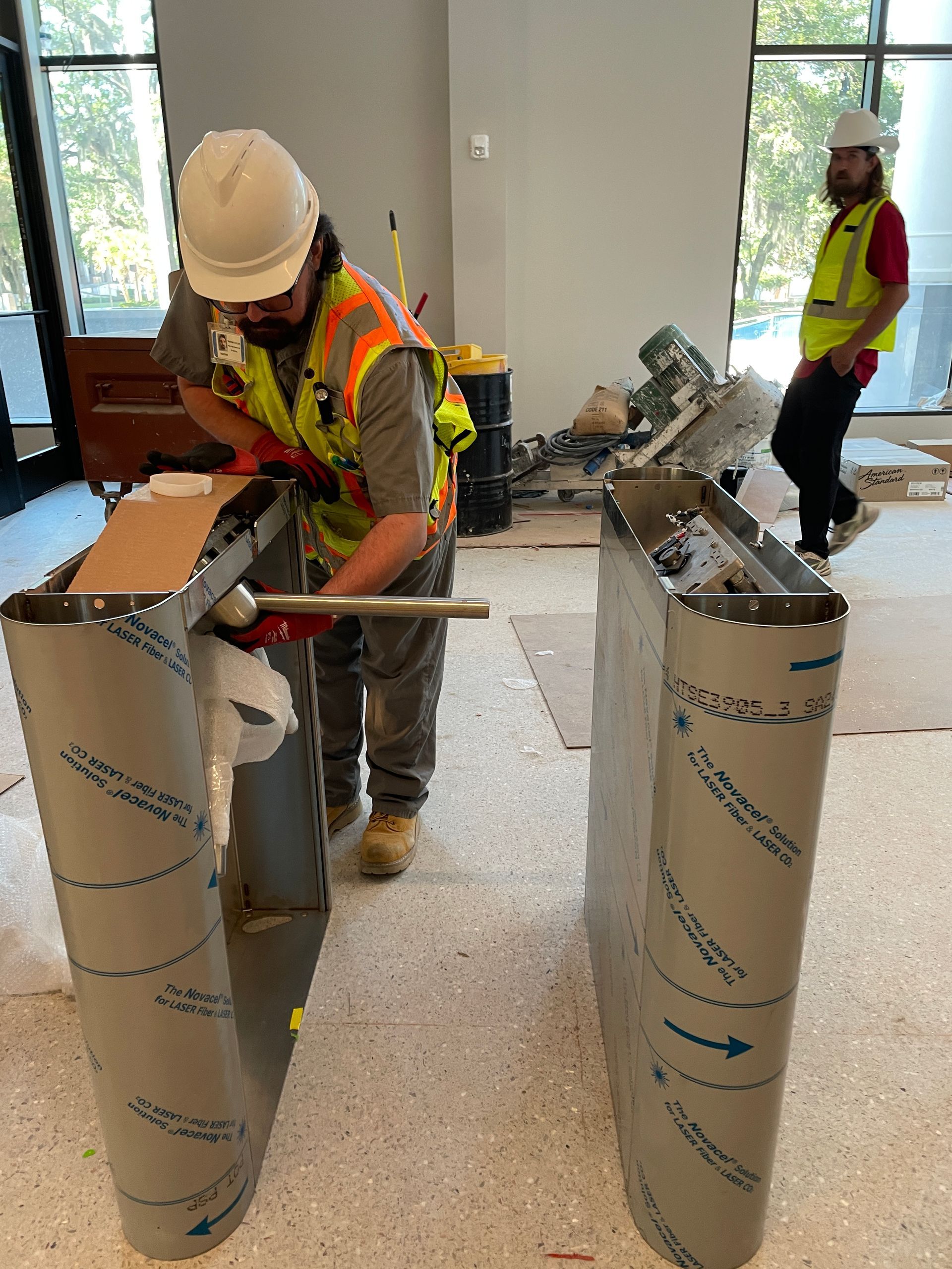 Two construction workers installing a metal structure indoors. 