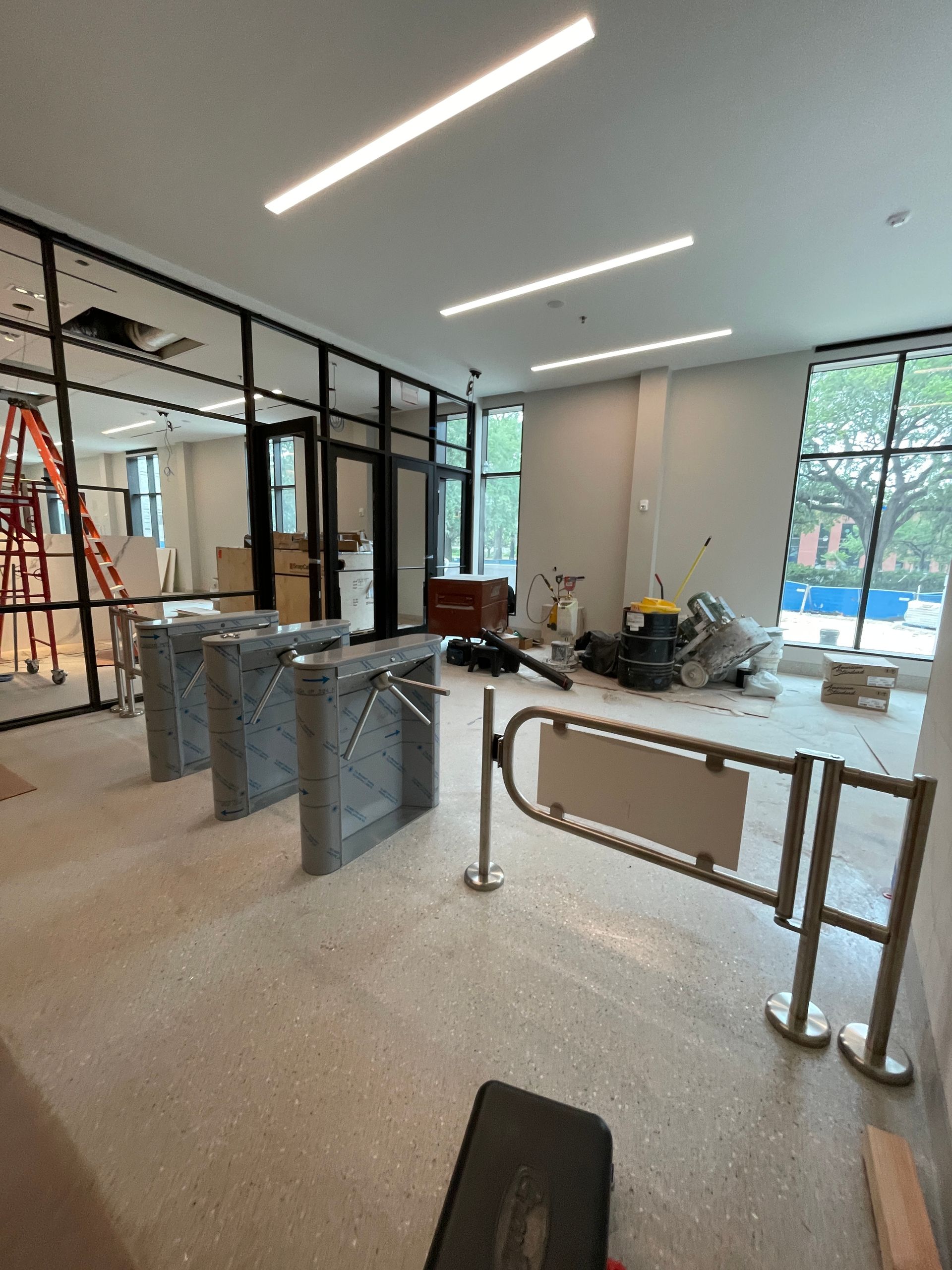 Construction site with gray turnstiles, glass walls, and a metal security gate. 