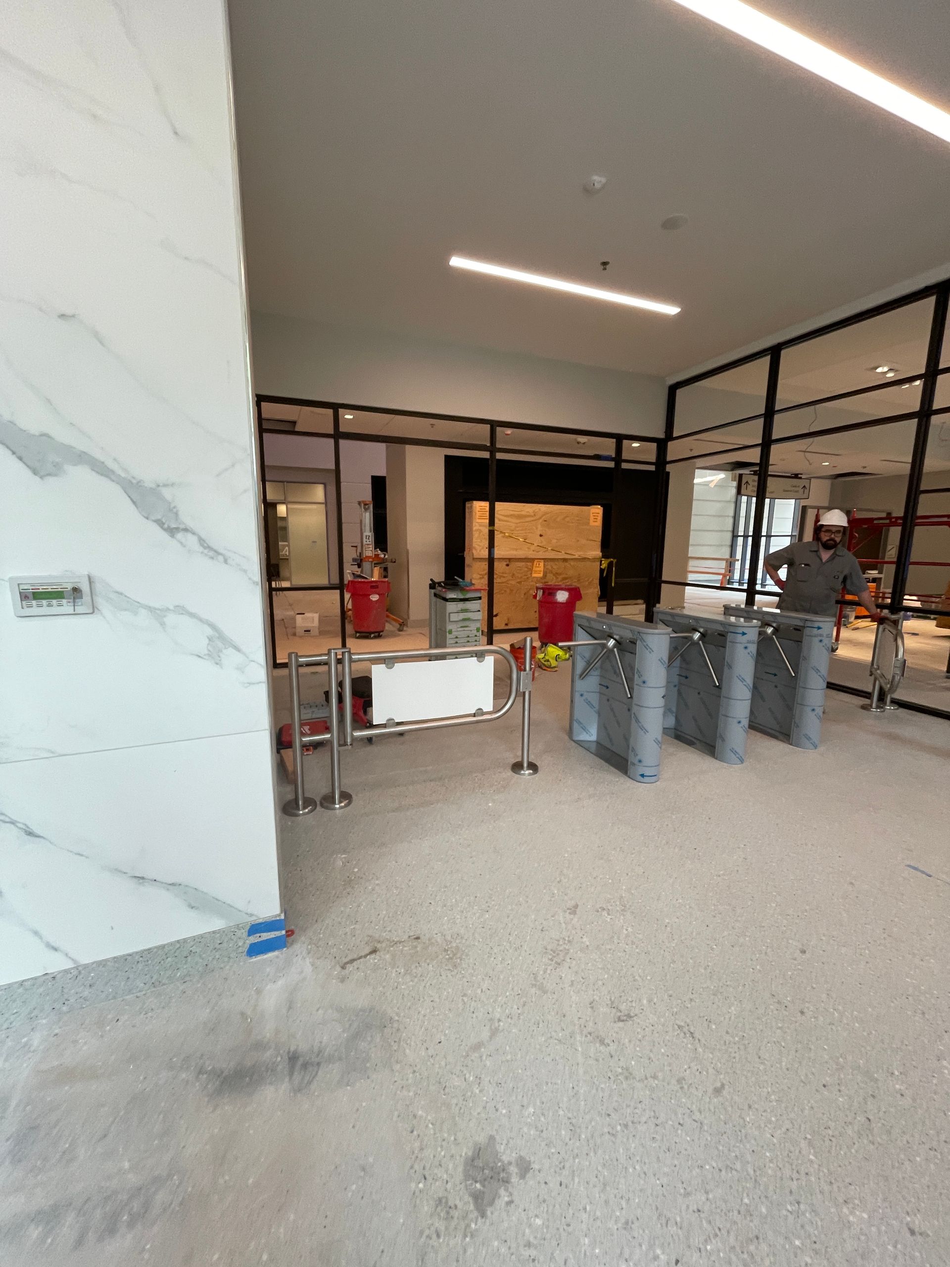 Lobby under construction with turnstiles, fire extinguishers, and marble wall. 