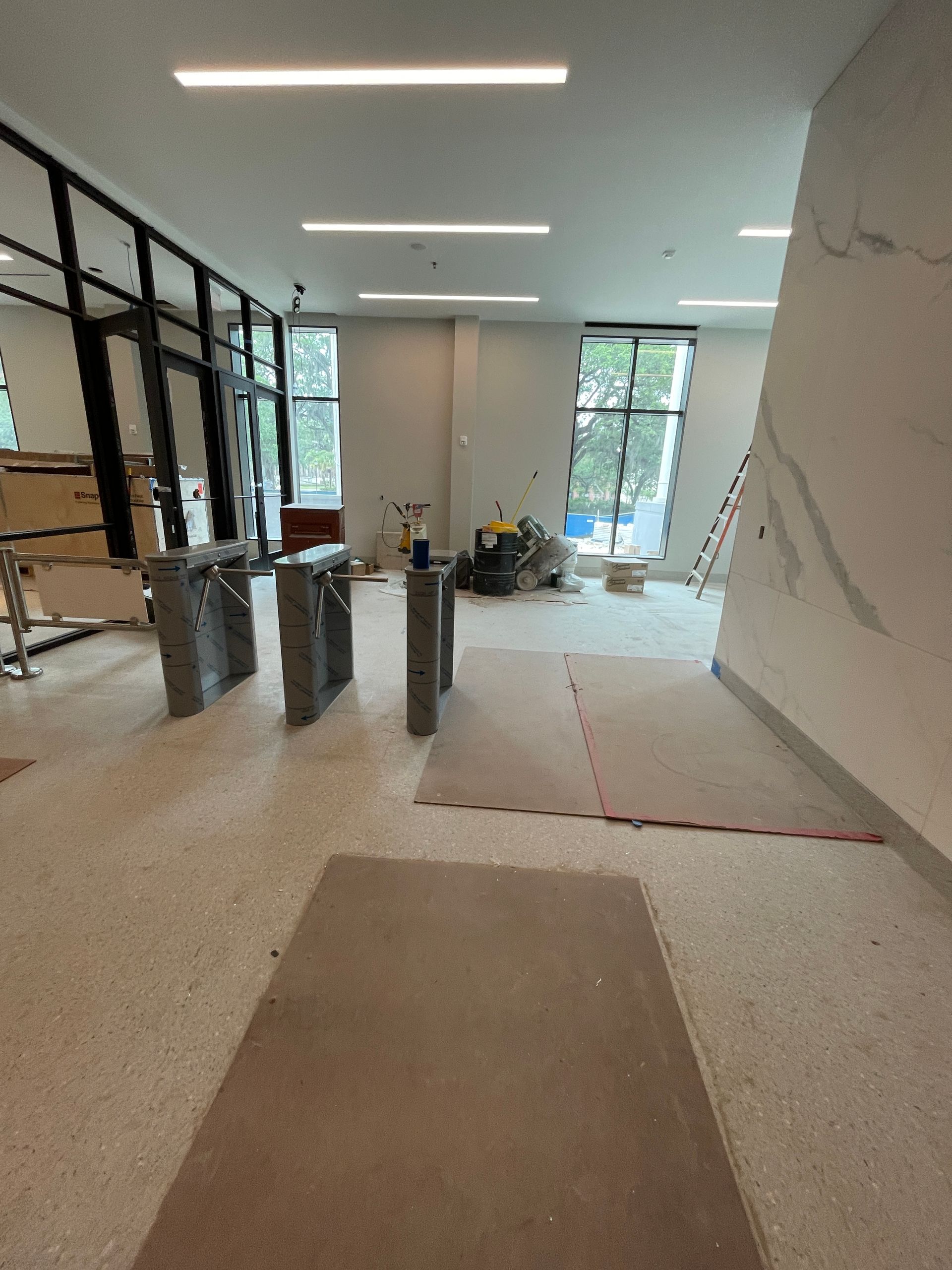 Interior view of a modern lobby under construction, featuring turnstiles, windows, and exposed building materials.