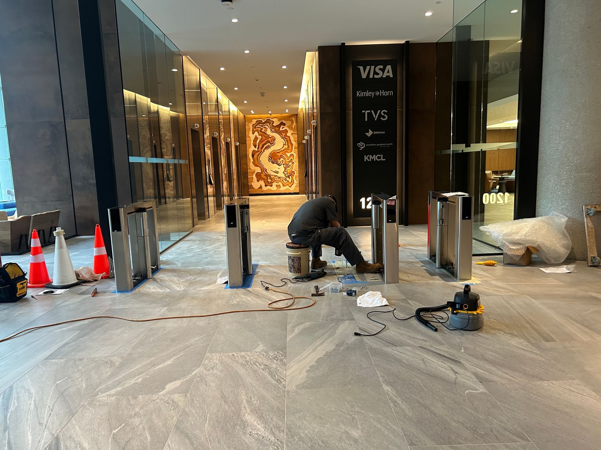 Person installing security turnstiles in a modern lobby.