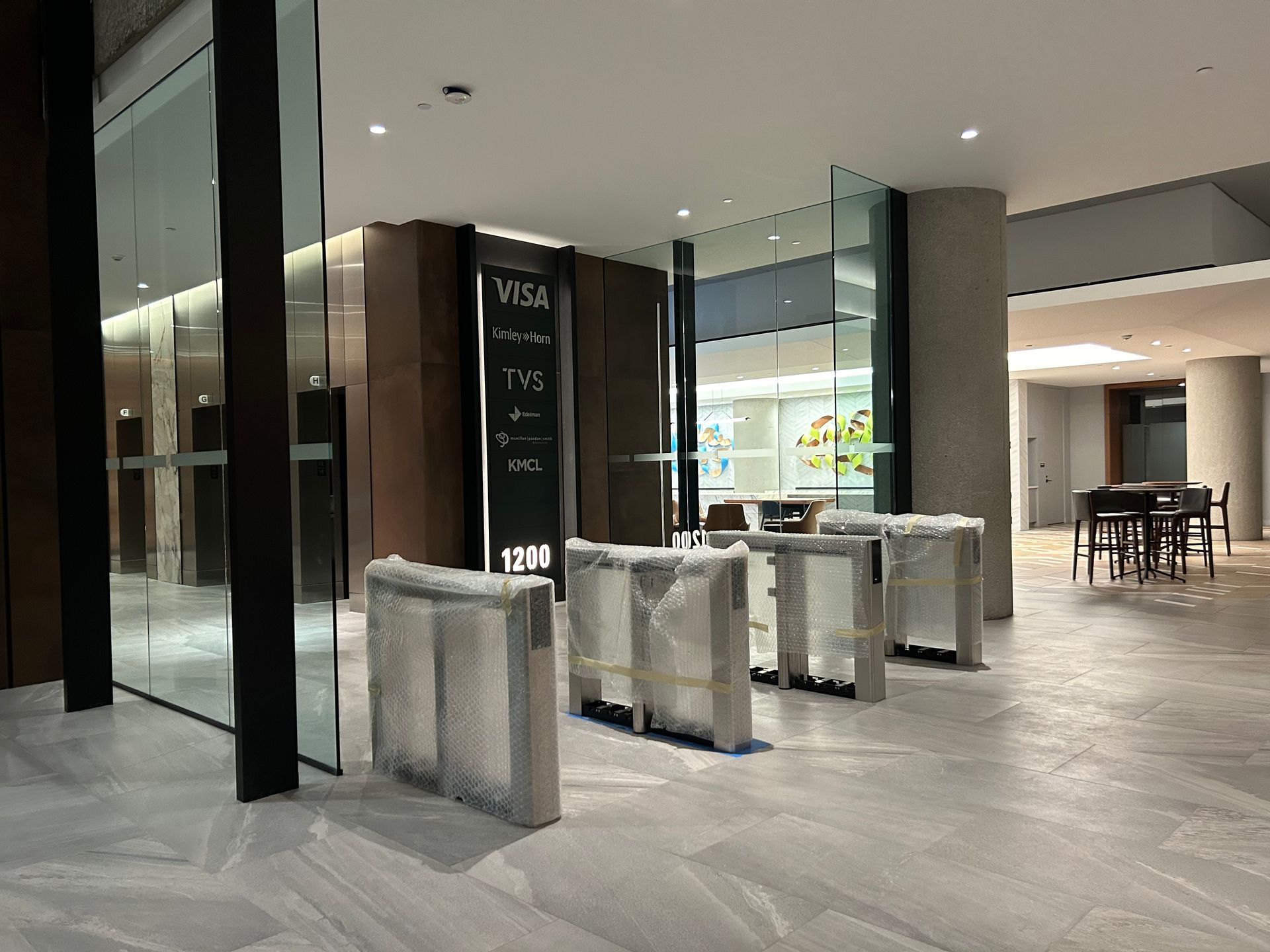 Lobby entrance with wrapped security turnstiles, glass walls, a service desk, and a seating area.